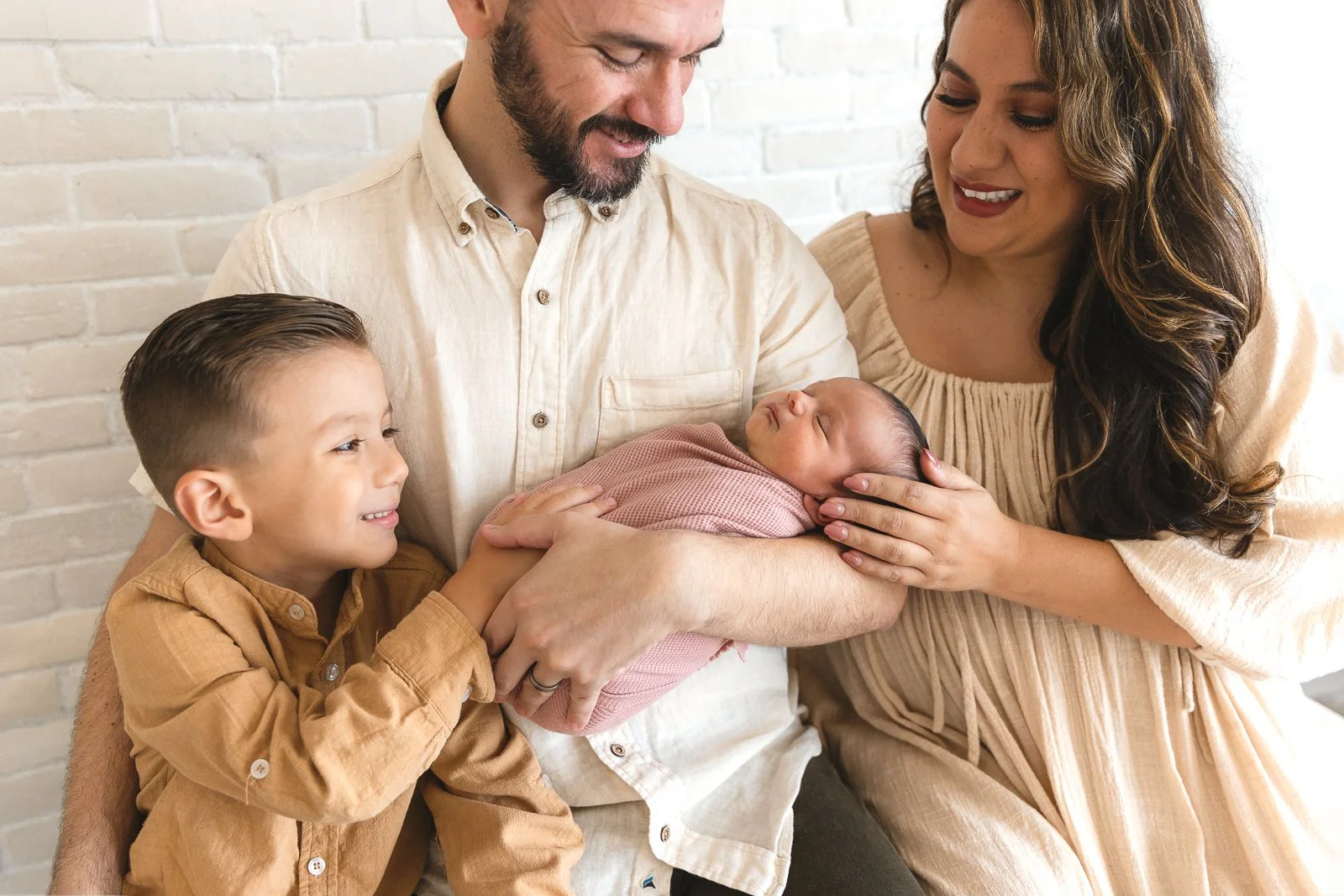 Family of four wearing coordinated warm neutral tones smiling at their newborn baby during a studio newborn session