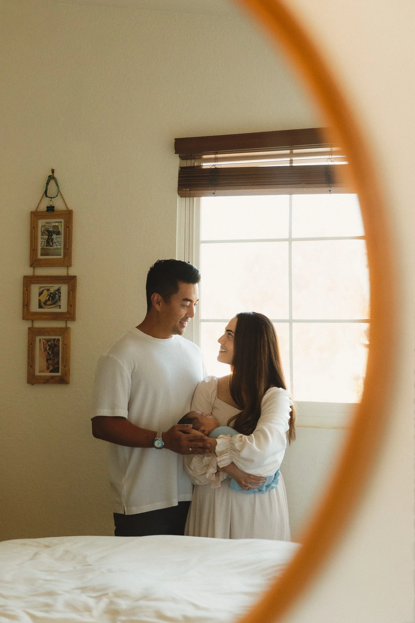 Parents standing by a window looking at each other while holding their newborn during an in-home newborn session in Orange County
