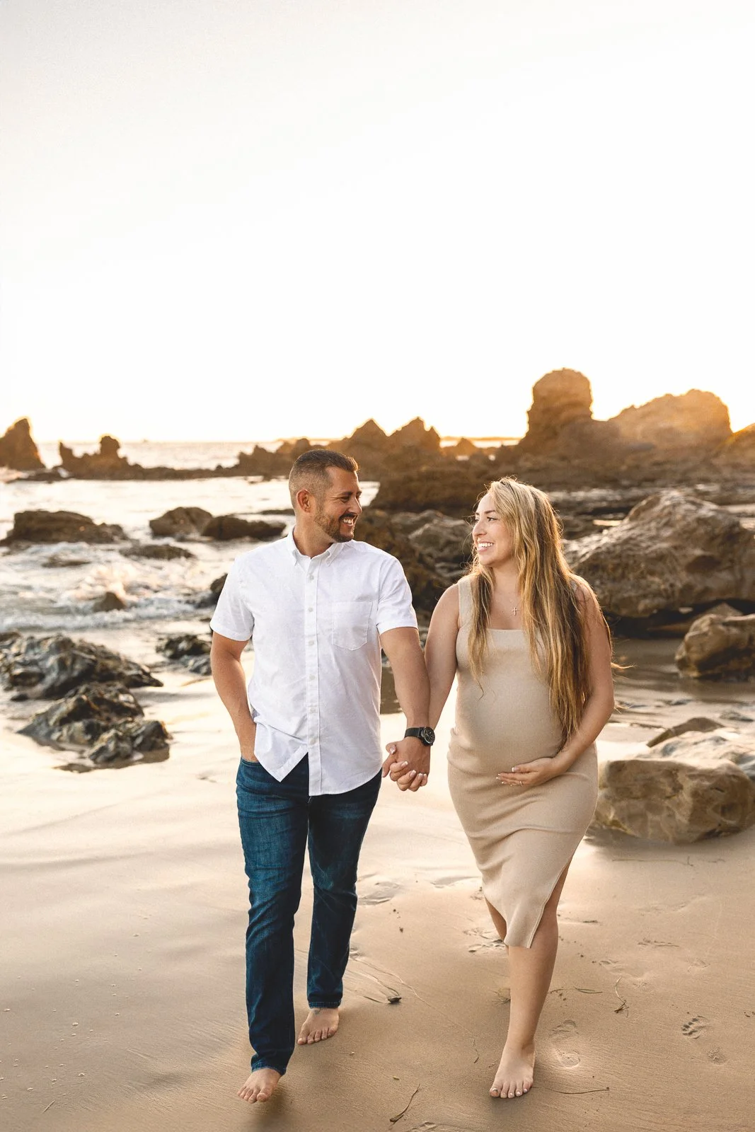 Pregnant couple walking hand in hand along the beach during a third trimester maternity session in Orange County