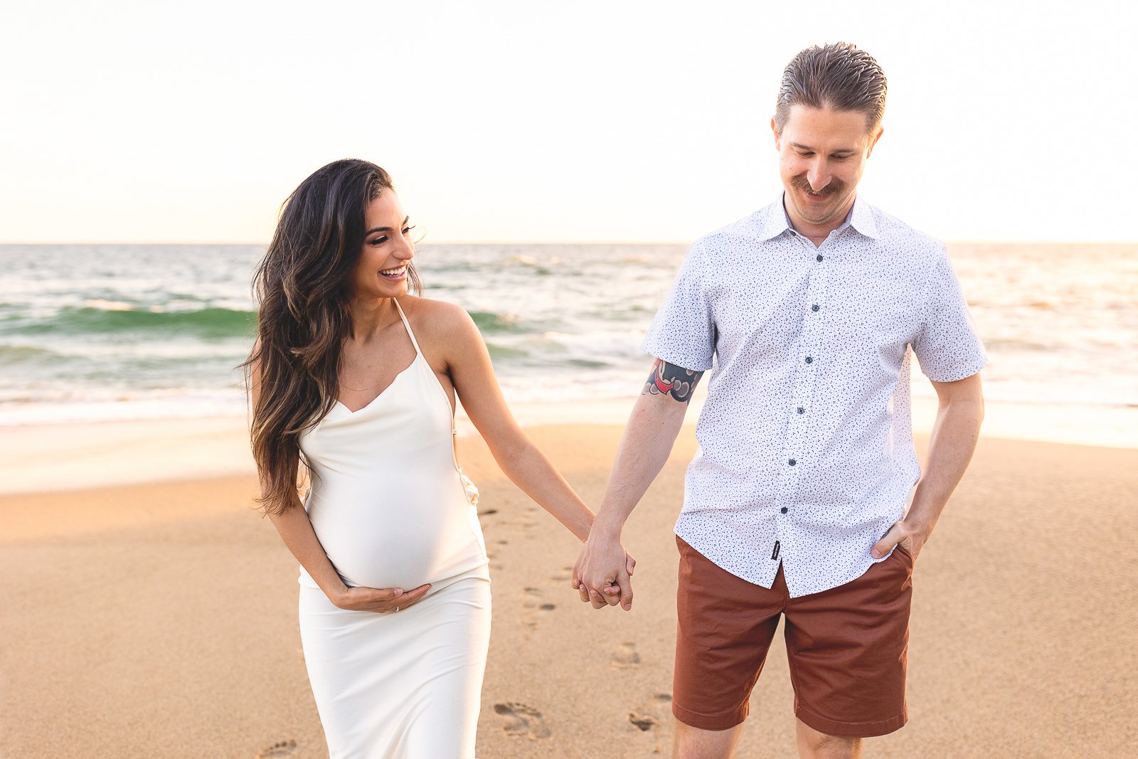 Orange County maternity photographer capturing a couple walking hand-in-hand on the beach.