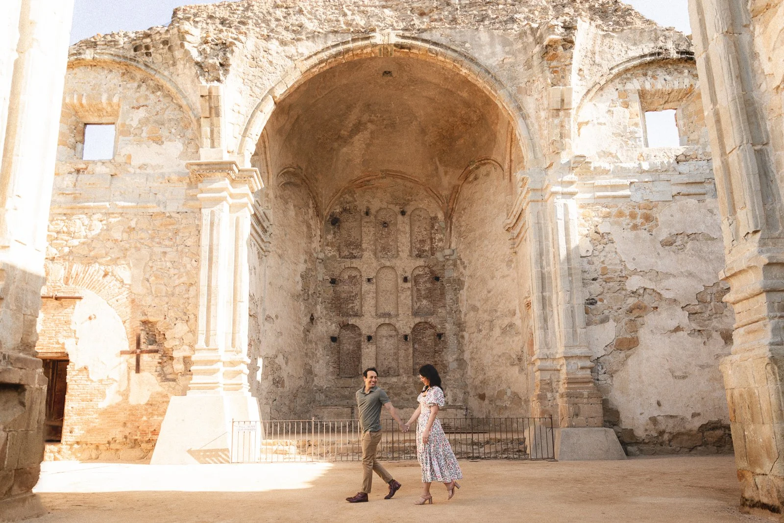Couple walking beneath the large stone arch inside Mission San Juan Capistrano in San Juan Capistrano, a classic Orange County photo location.