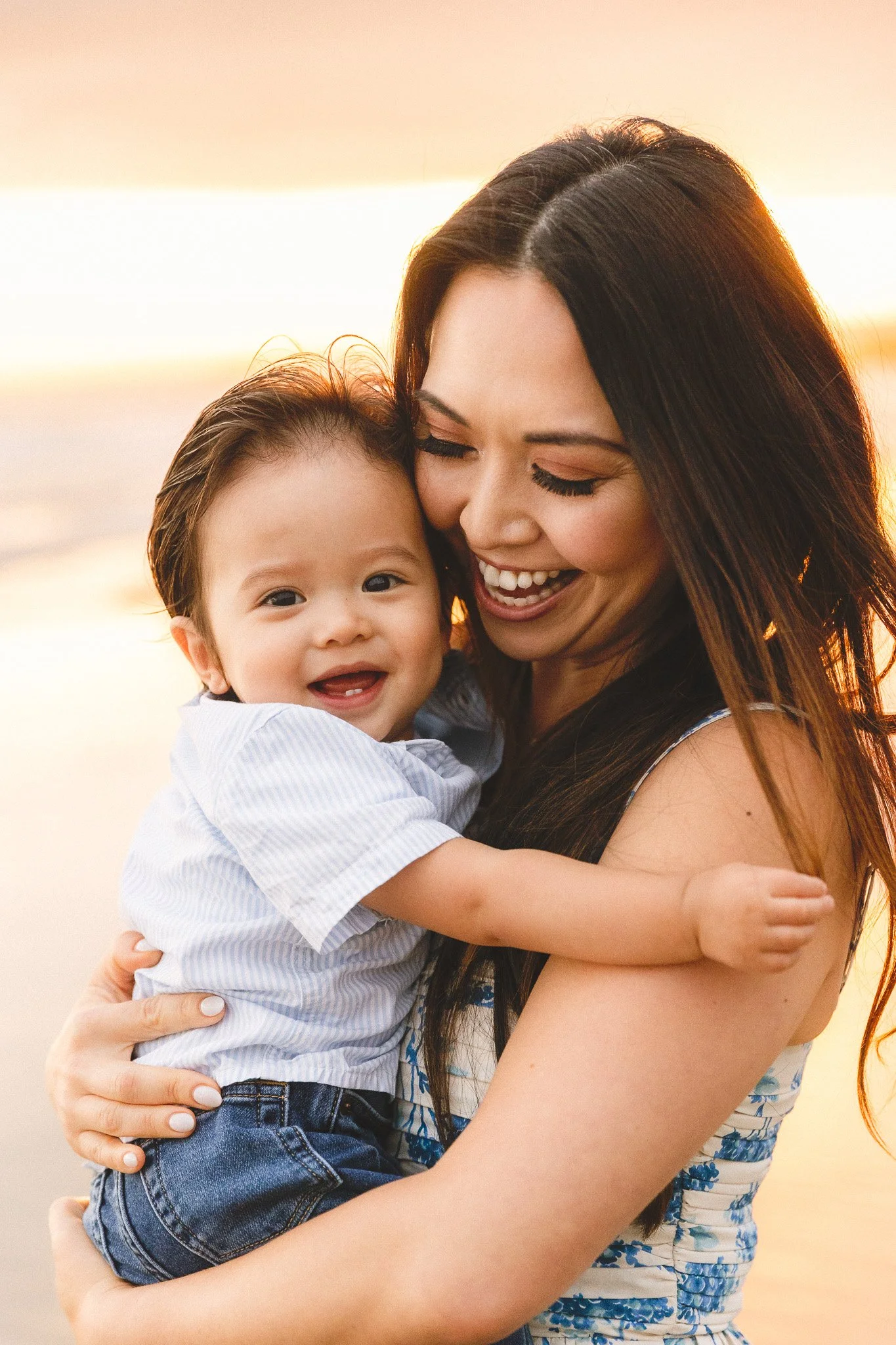 Outdoor family photoshoot with a toddler in Orange County. Mom snuggles her smiling toddler son close at golden hour, both laughing together.