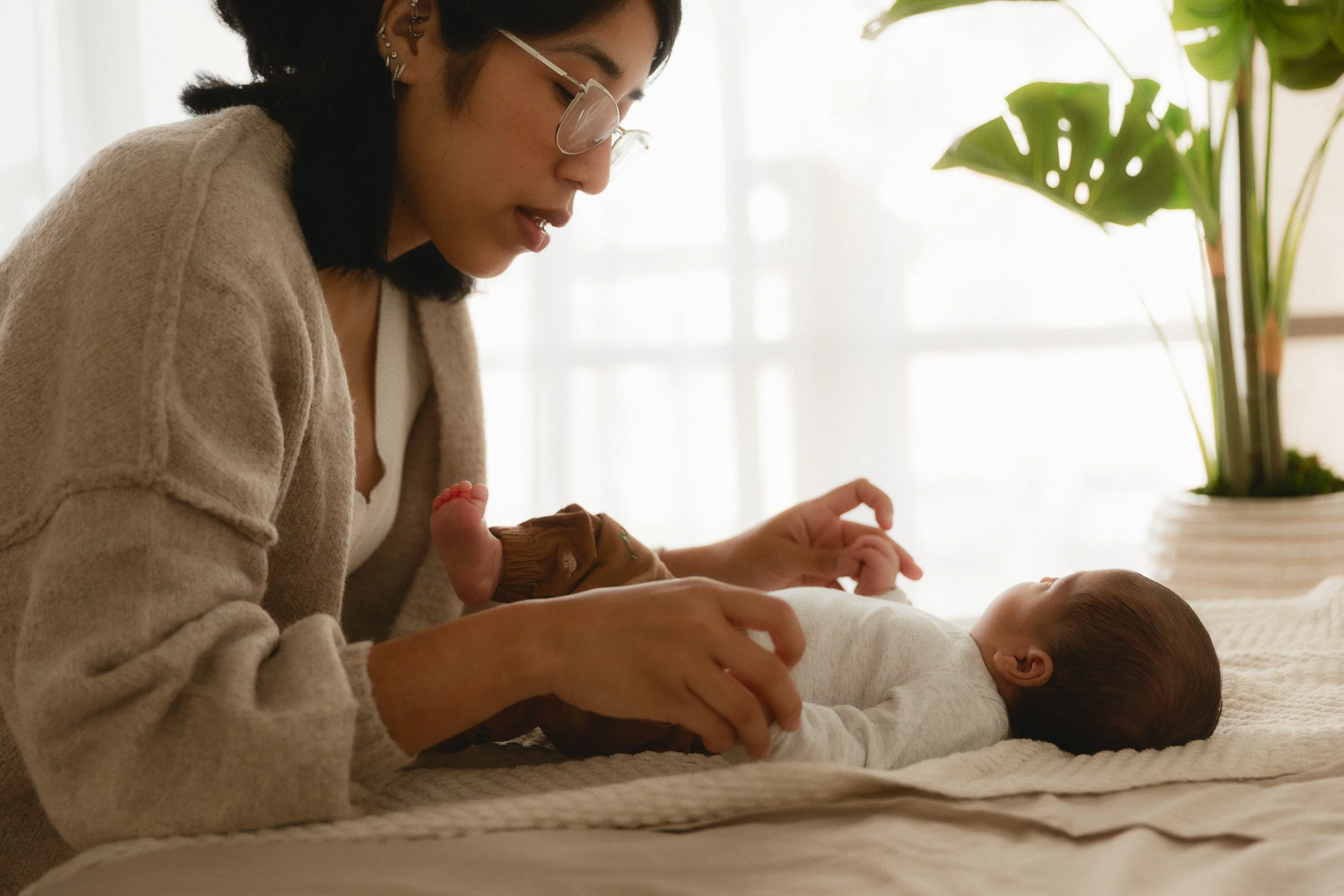 Mom leaning over her newborn baby on a soft blanket during a baby-led newborn session at Spark Studios in Huntington Beach