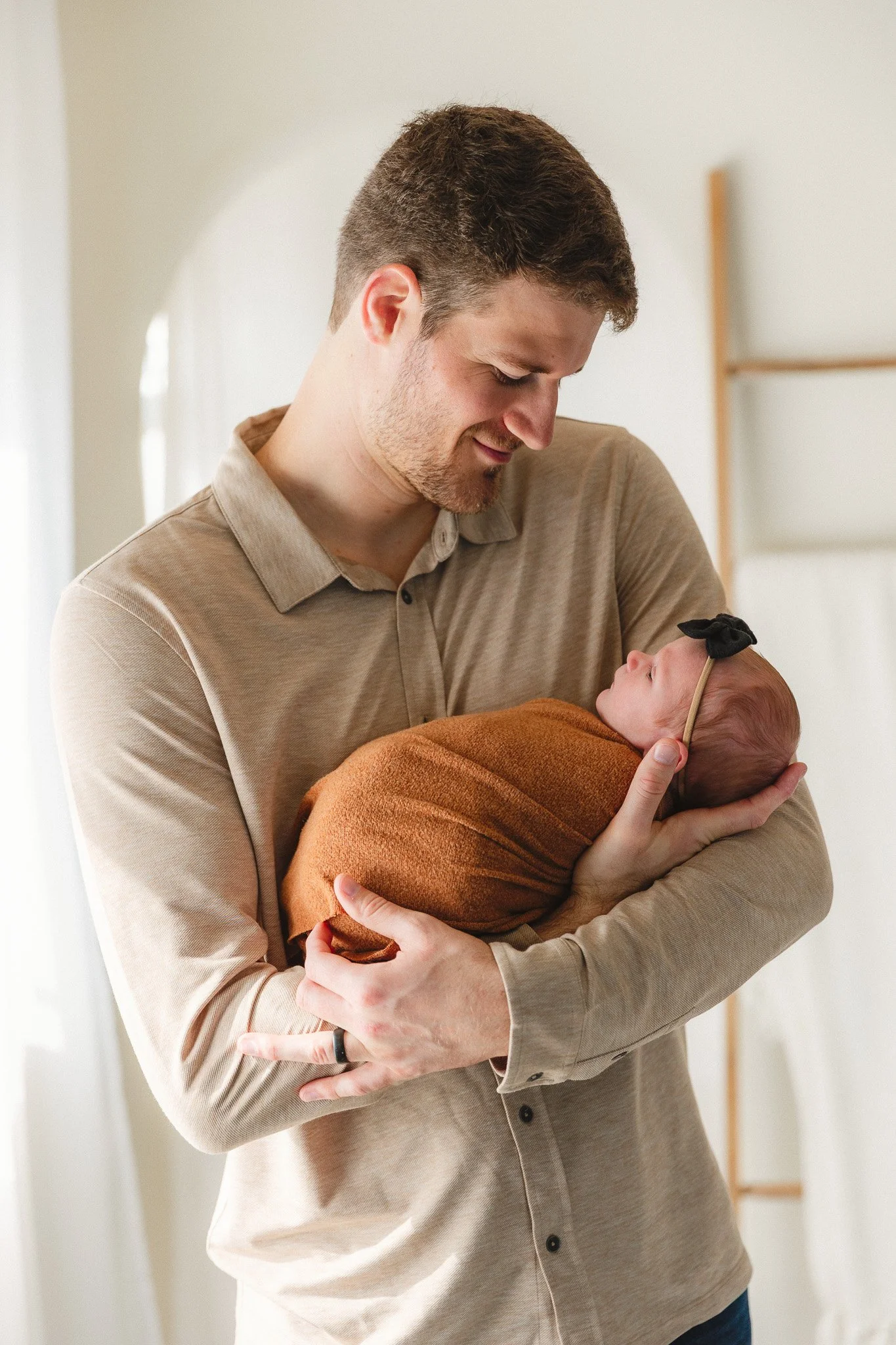 Dad wearing a soft tan polo shirt holding his swaddled newborn during a newborn photography session
