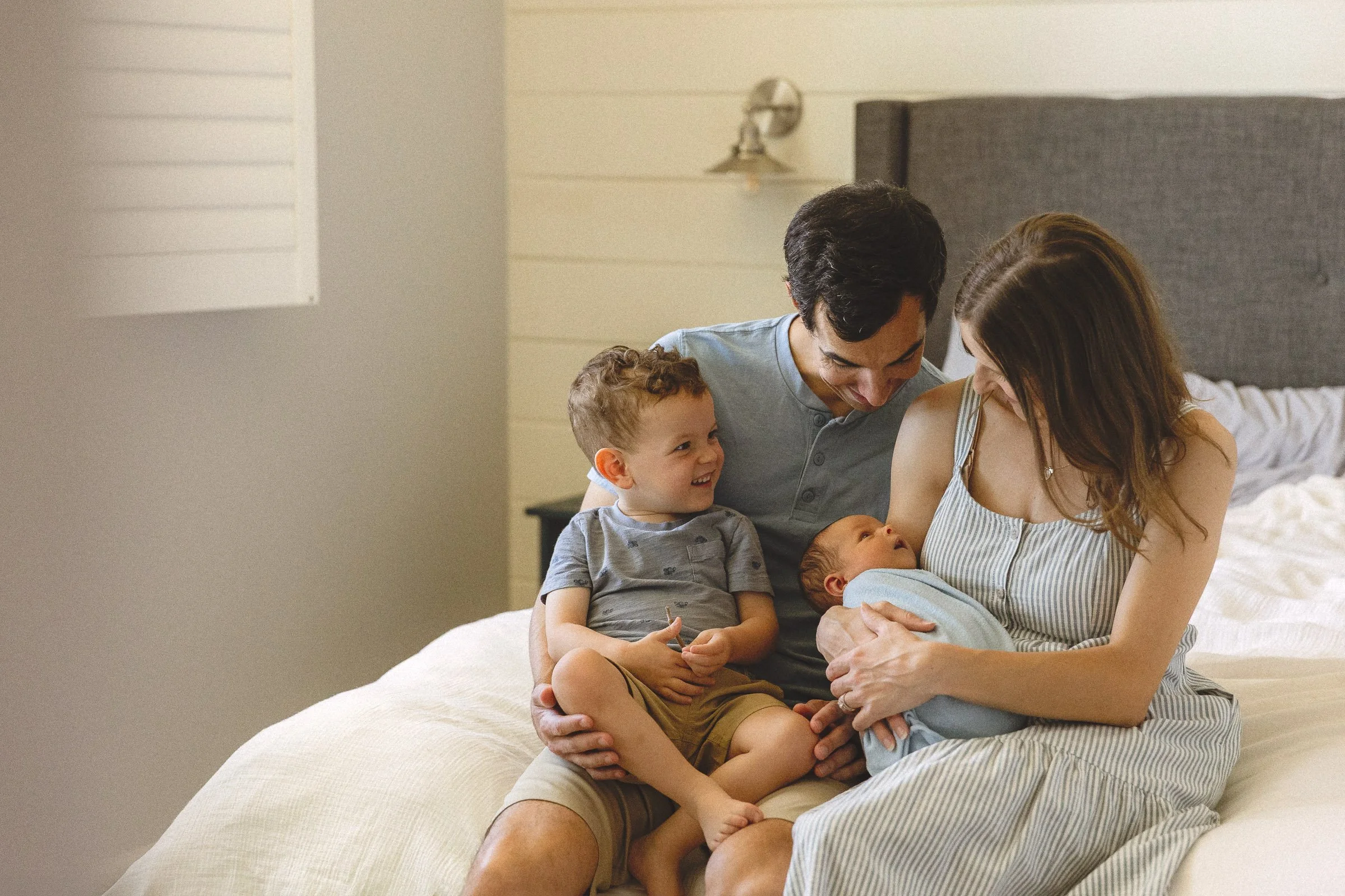 Family with toddler and newborn sitting on a bed together during an in-home newborn photography session in Orange County