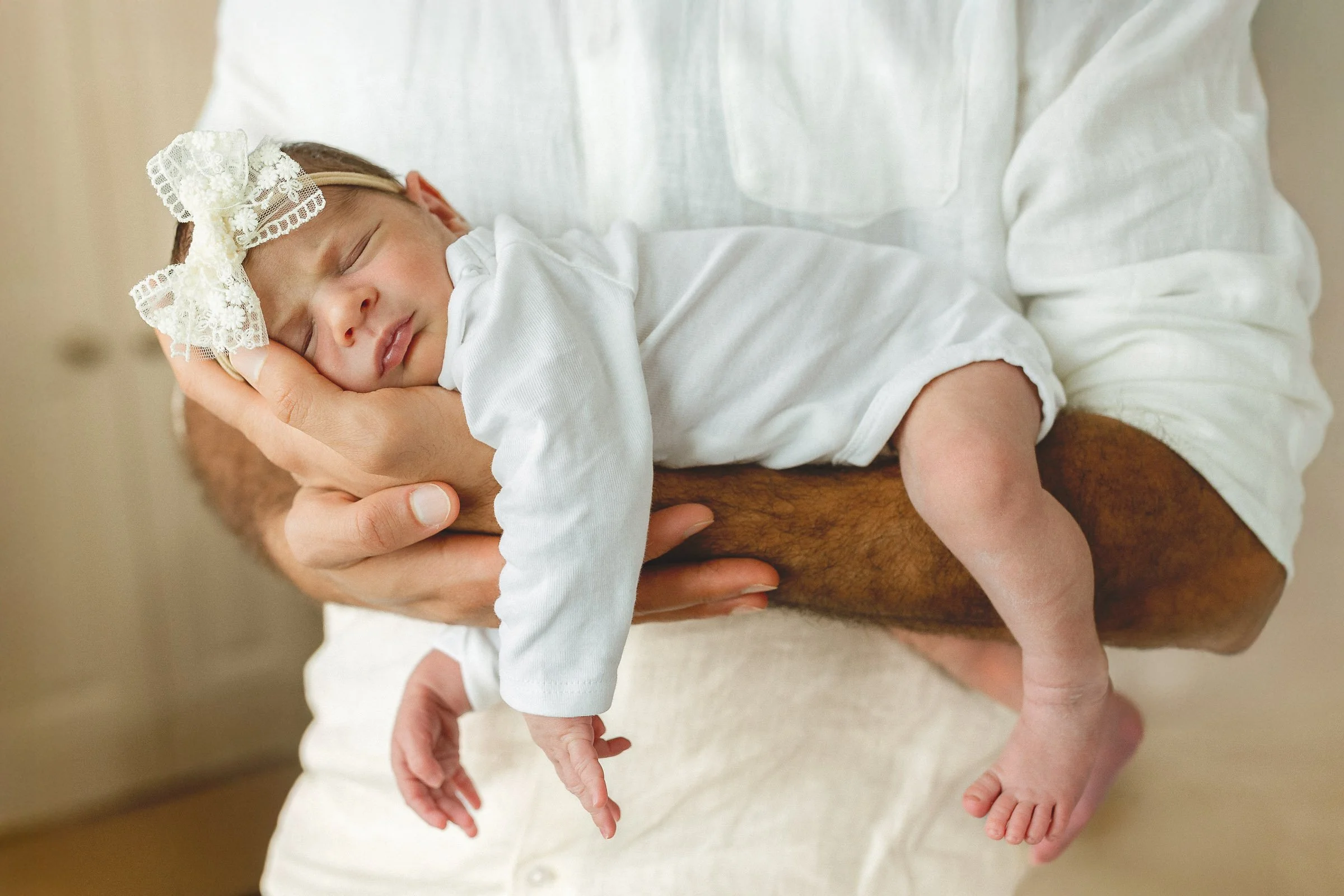 Sleeping newborn cradled in a parent’s arms in soft window light, Orange County newborn photographer.