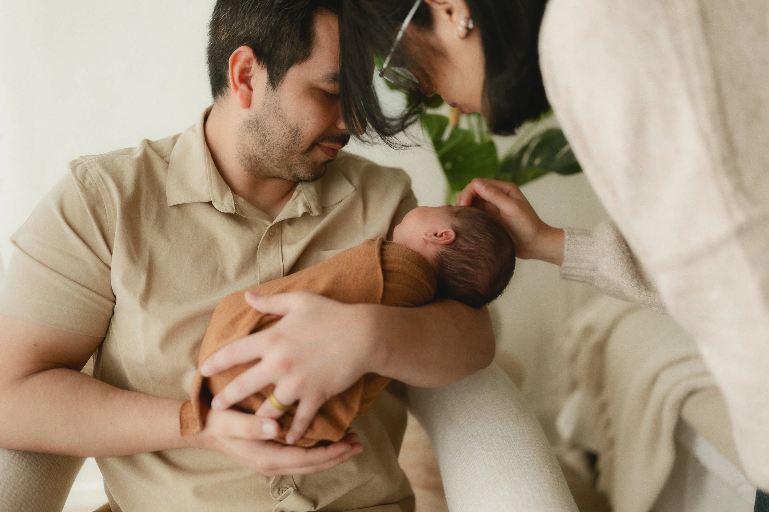 Dad holding newborn while mom reaches in to touch the baby during a natural light newborn session at Spark Studios
