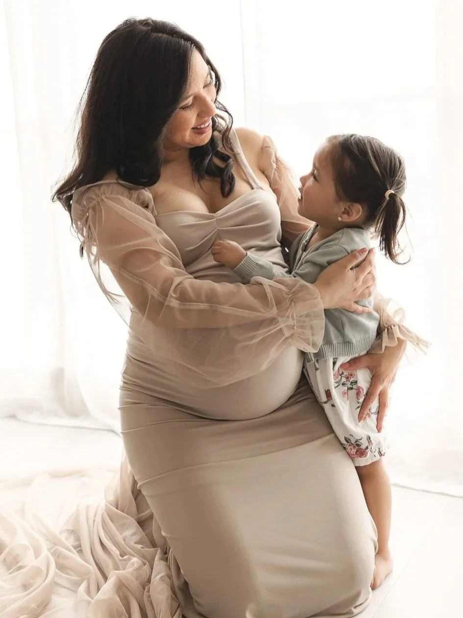 Expecting mom holding her toddler during a studio maternity session in soft window light.
