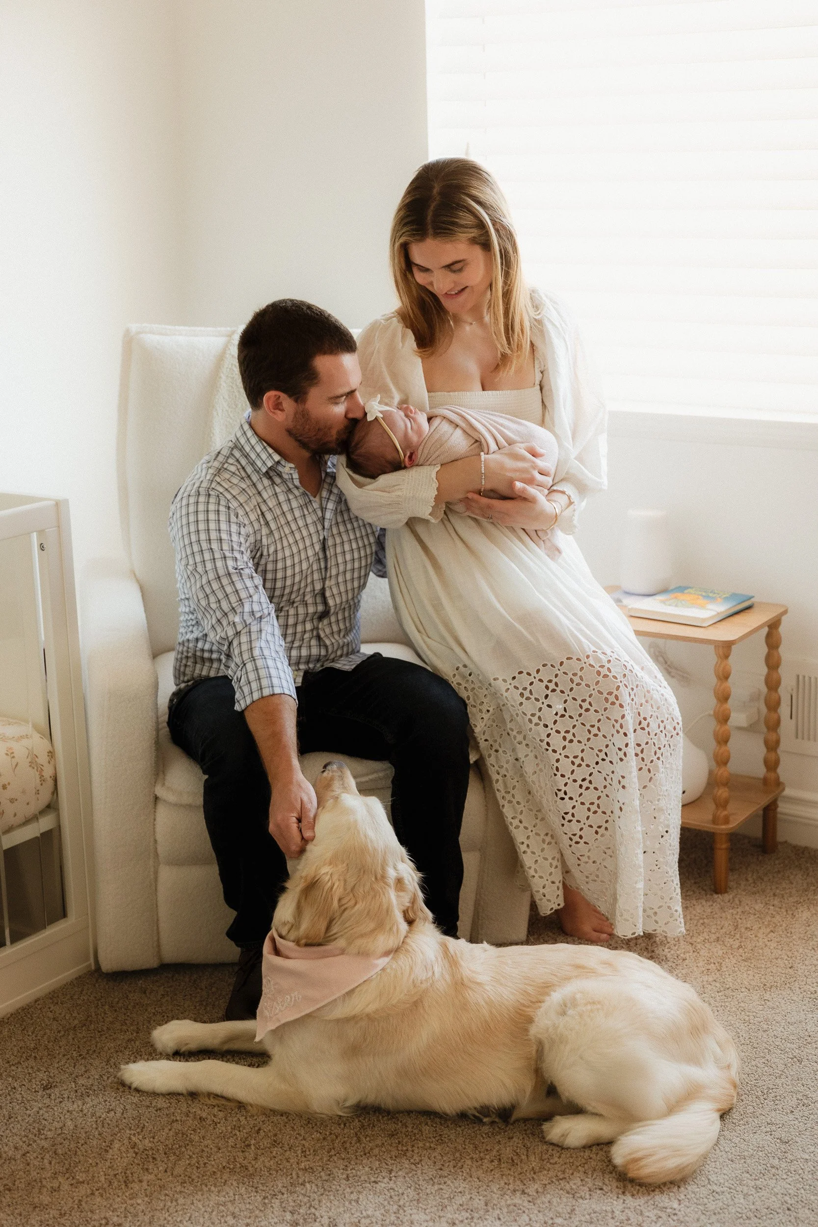 Parents holding their newborn in the nursery while their golden retriever sits nearby during an in-home newborn session in Orange County