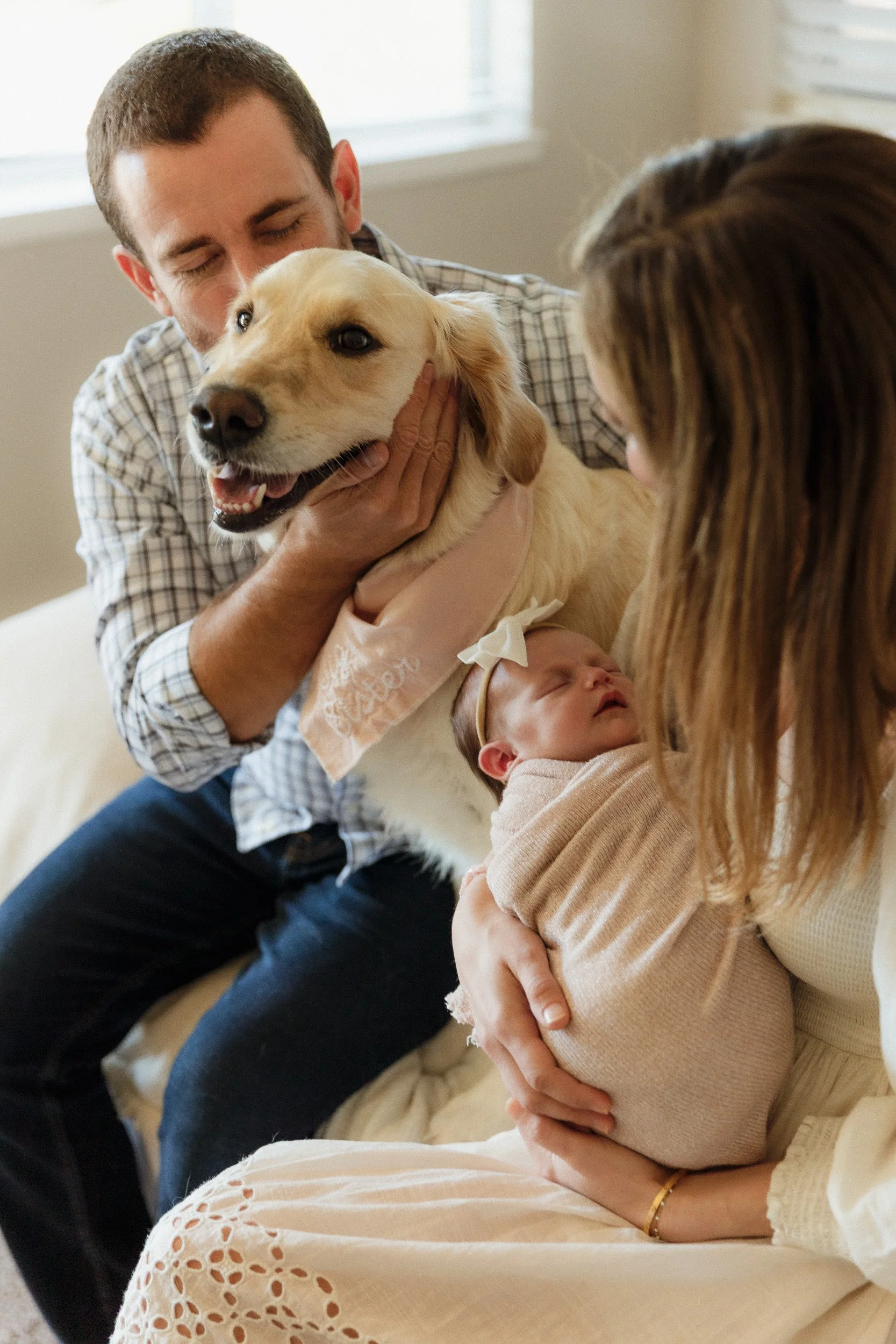 Newborn photography session including the family dog in Orange County. Dad gently holds the golden retriever while mom cradles their newborn baby in a soft pink wrap.