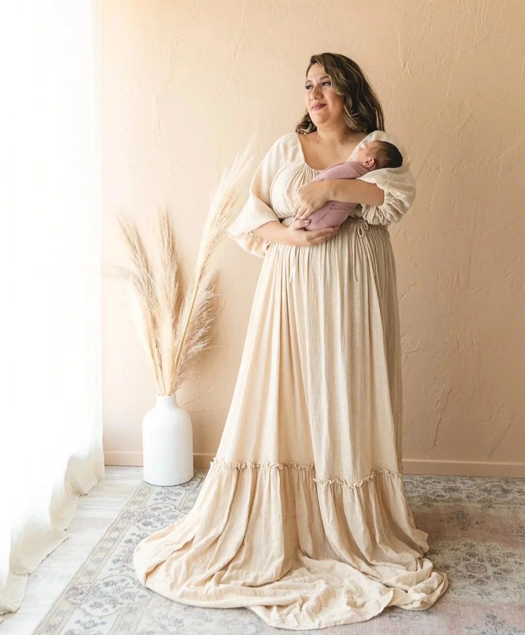 Mom wearing a long cream flowy dress holding her swaddled newborn during a studio newborn session