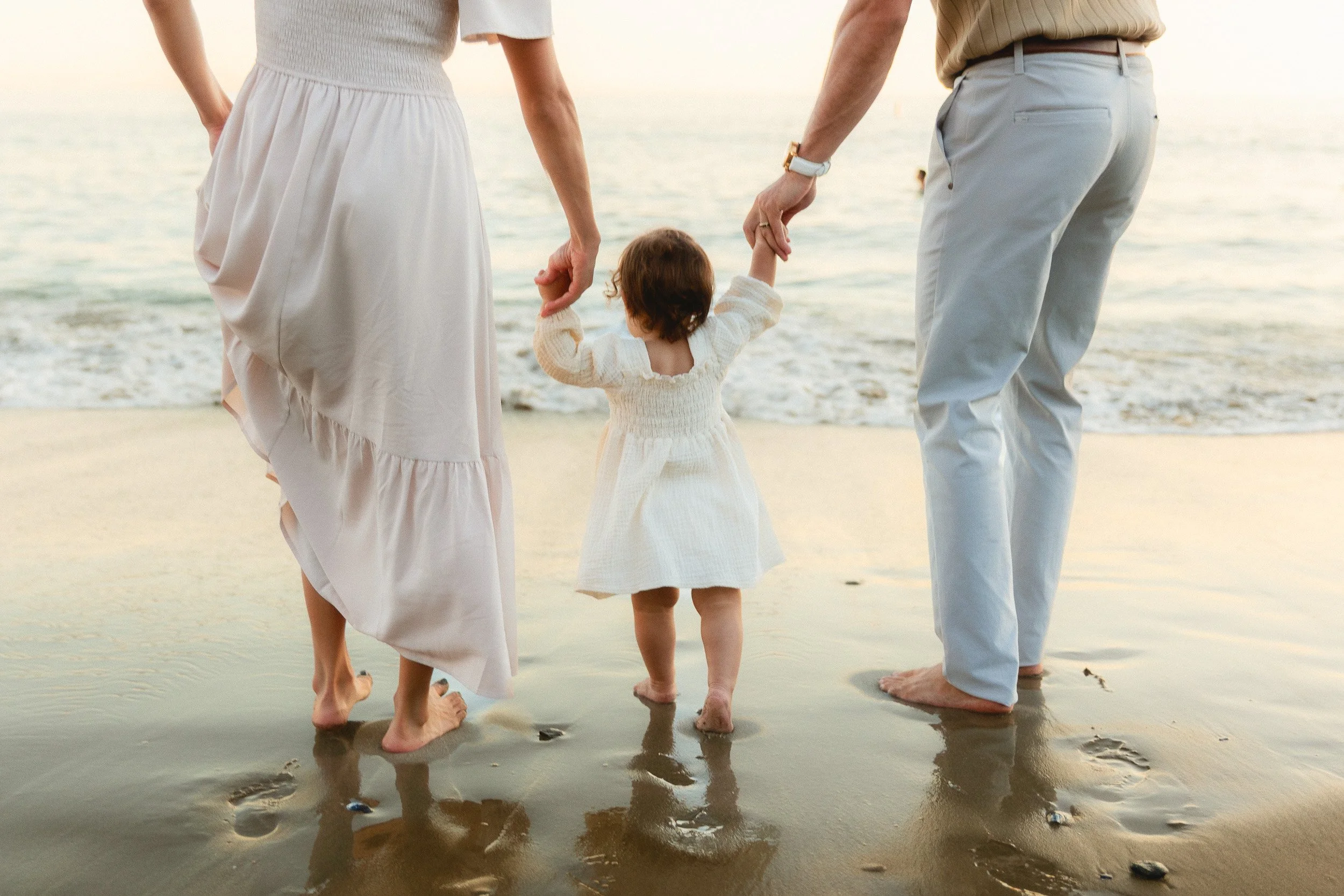 Orange County family photographer session with parents and toddler walking hand in hand on the beach