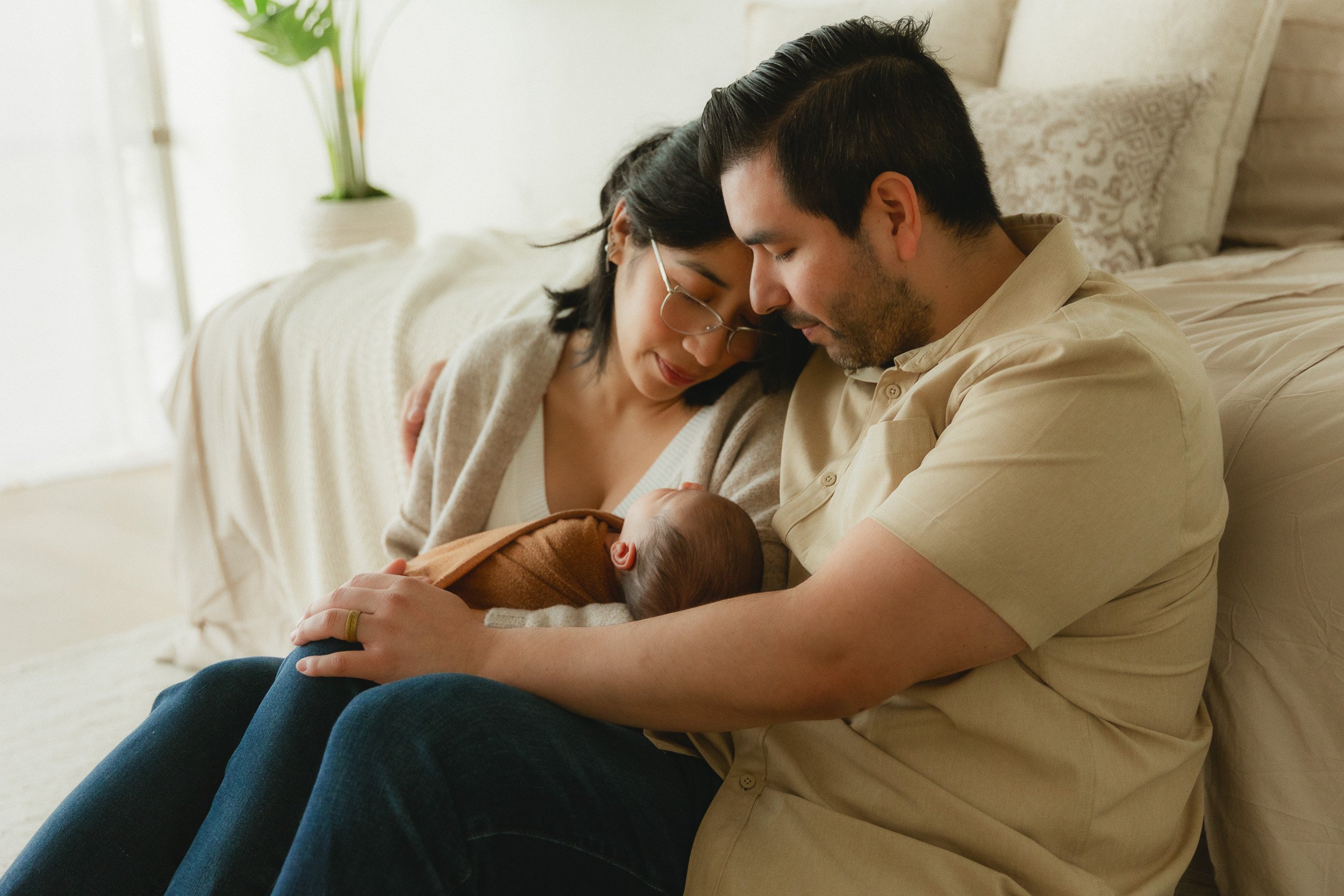 Mom and dad snuggling their newborn on a couch during a studio newborn photography session at Spark Studios in Huntington Beach