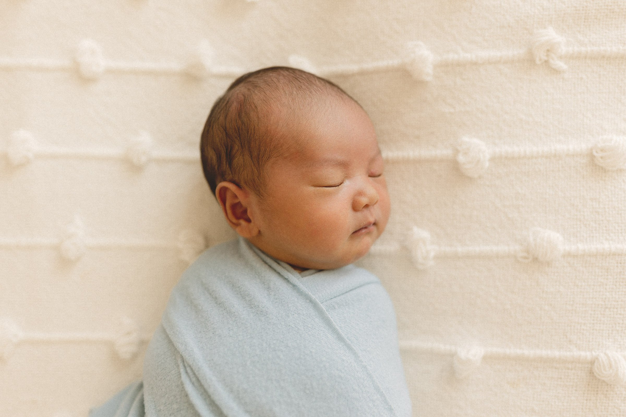 Swaddled newborn sleeping in a close-up portrait with soft neutral tones.