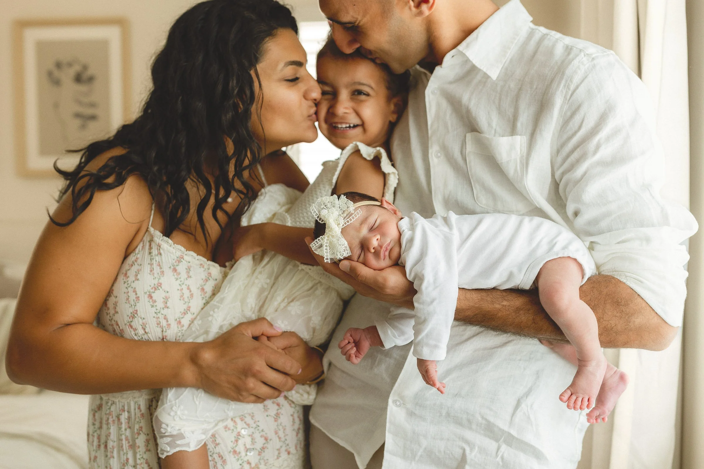 Parents kissing their toddler while dad holds their sleeping newborn during a newborn session in Orange County