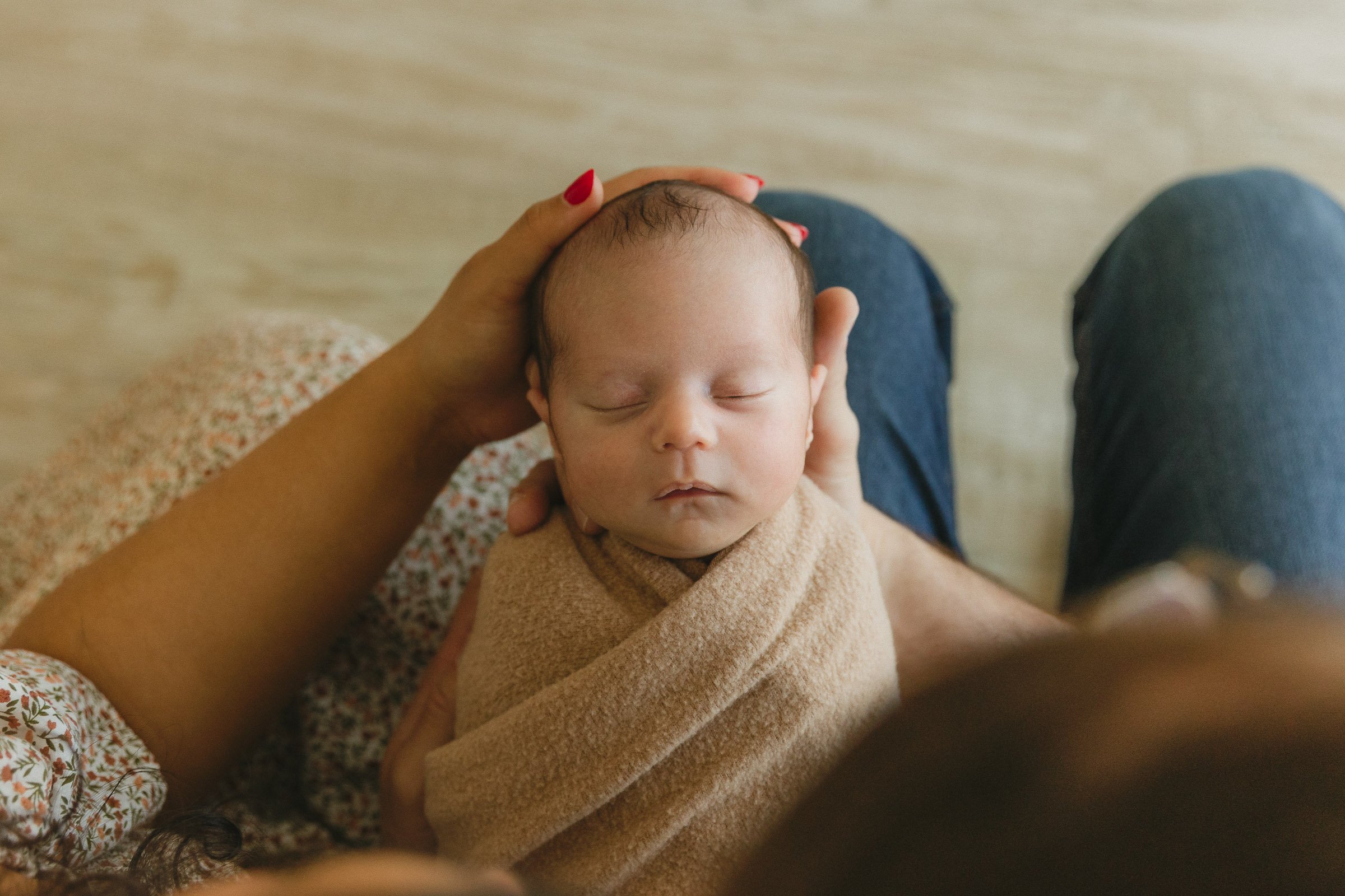Mom gently cradling the head of her swaddled newborn during a baby-led newborn photo session in Orange County