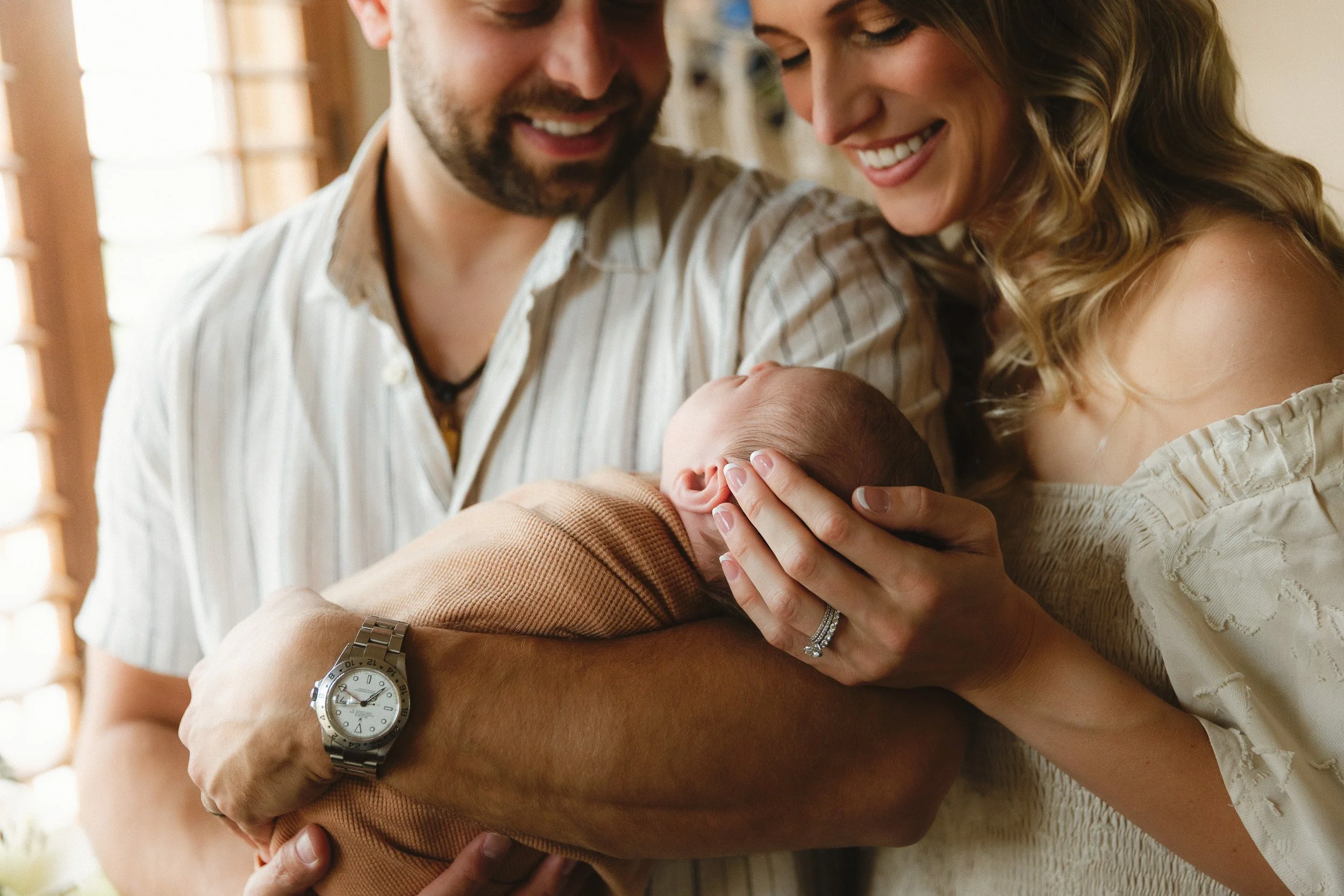 Rancho Santa Margarita newborn photographer in-home session with parents smiling and holding swaddled newborn