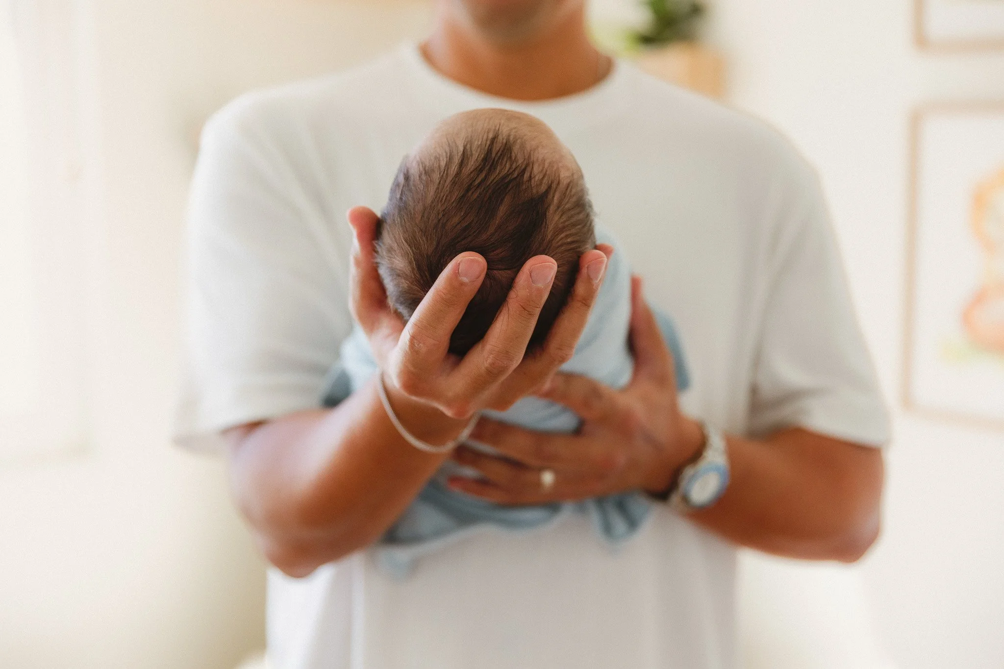 Close-up of a dad holding his newborn baby against his chest in soft window light.