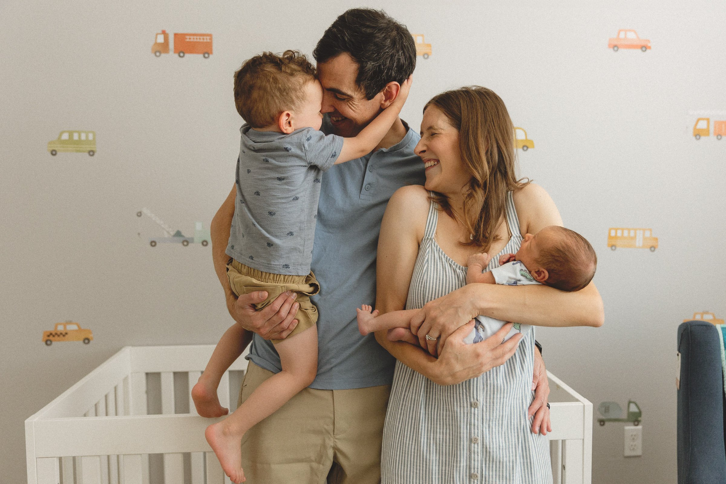 Family standing in their nursery with toddler and newborn wearing coordinated soft blue and neutral outfits during an in-home newborn session