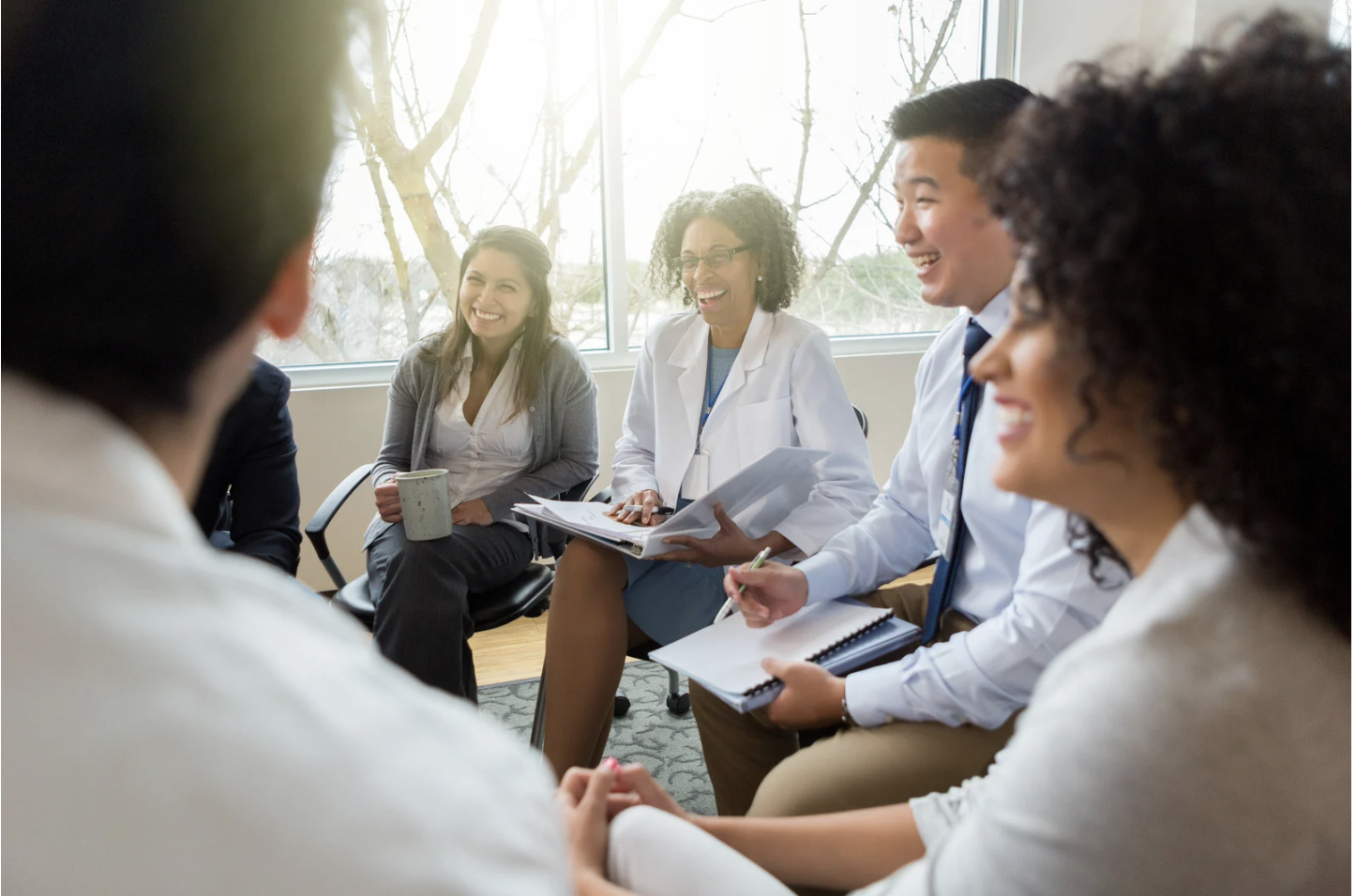 Medical professionals and a woman in a meeting room, all smiling and engaged in conversation during a discussion or team meeting.
