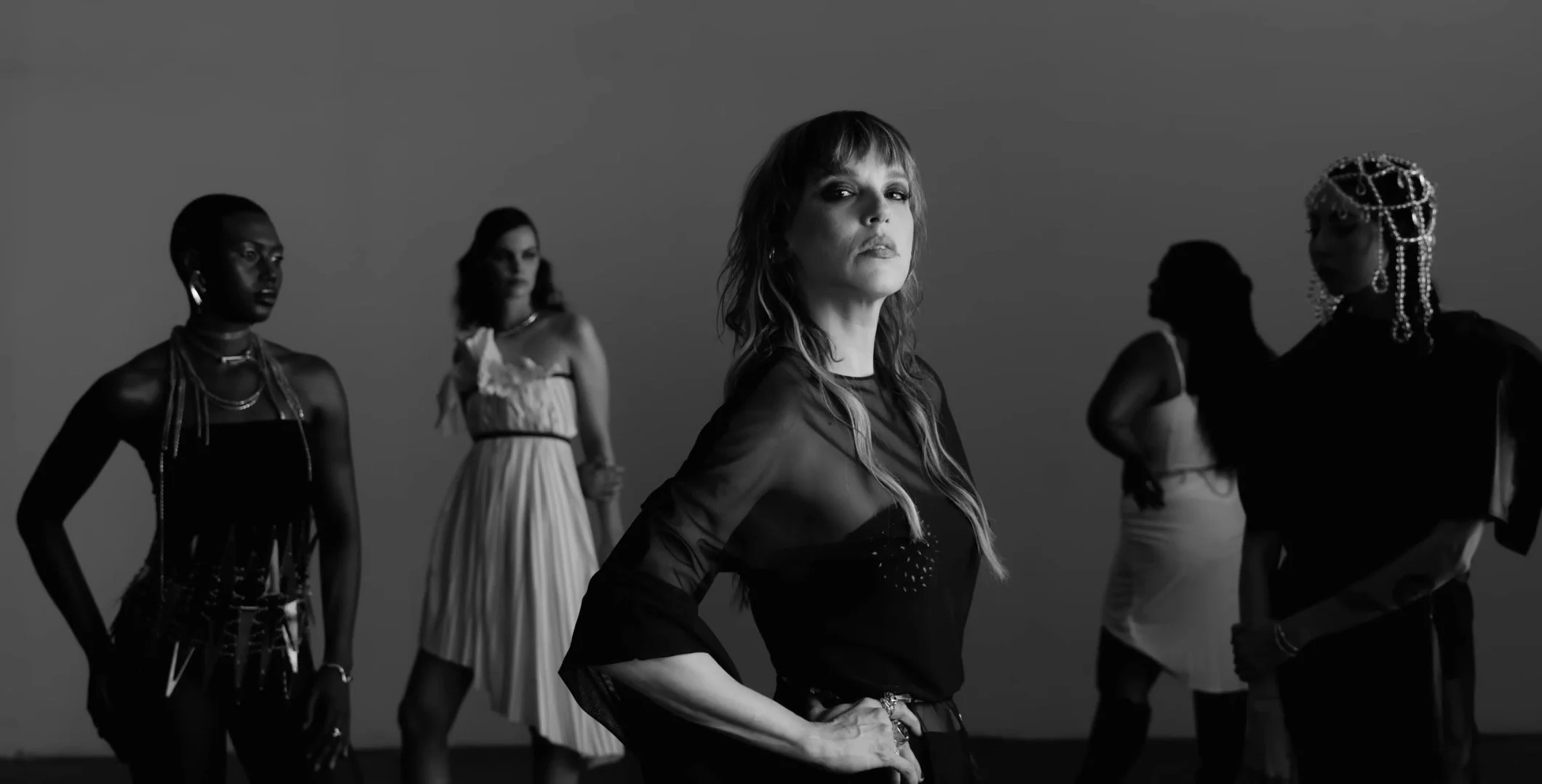 A black and white photo of five women posing, some wearing fashionable outfits and accessories, against a plain background.