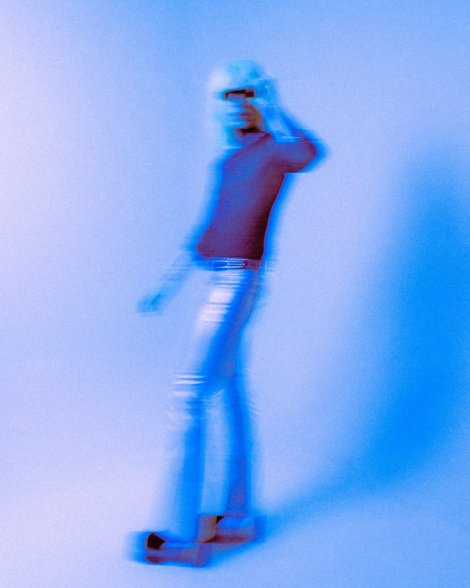 Person taking a photo or selfie in front of a mirror with a smartphone, wearing a white shirt and dark pants, with a blue background.