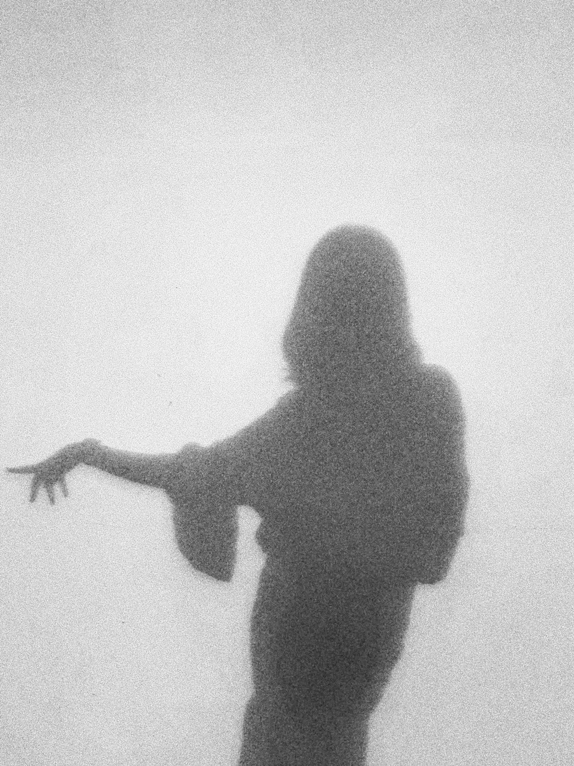 Black and white grainy silhouette of a person with long hair, holding a toy or object, against a plain background.