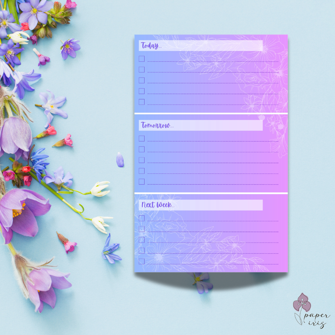 Wooden desk with a daily planner featuring floral designs, a latte with latte art, a pen, an open spiral notebook, a laptop, and a potted plant.