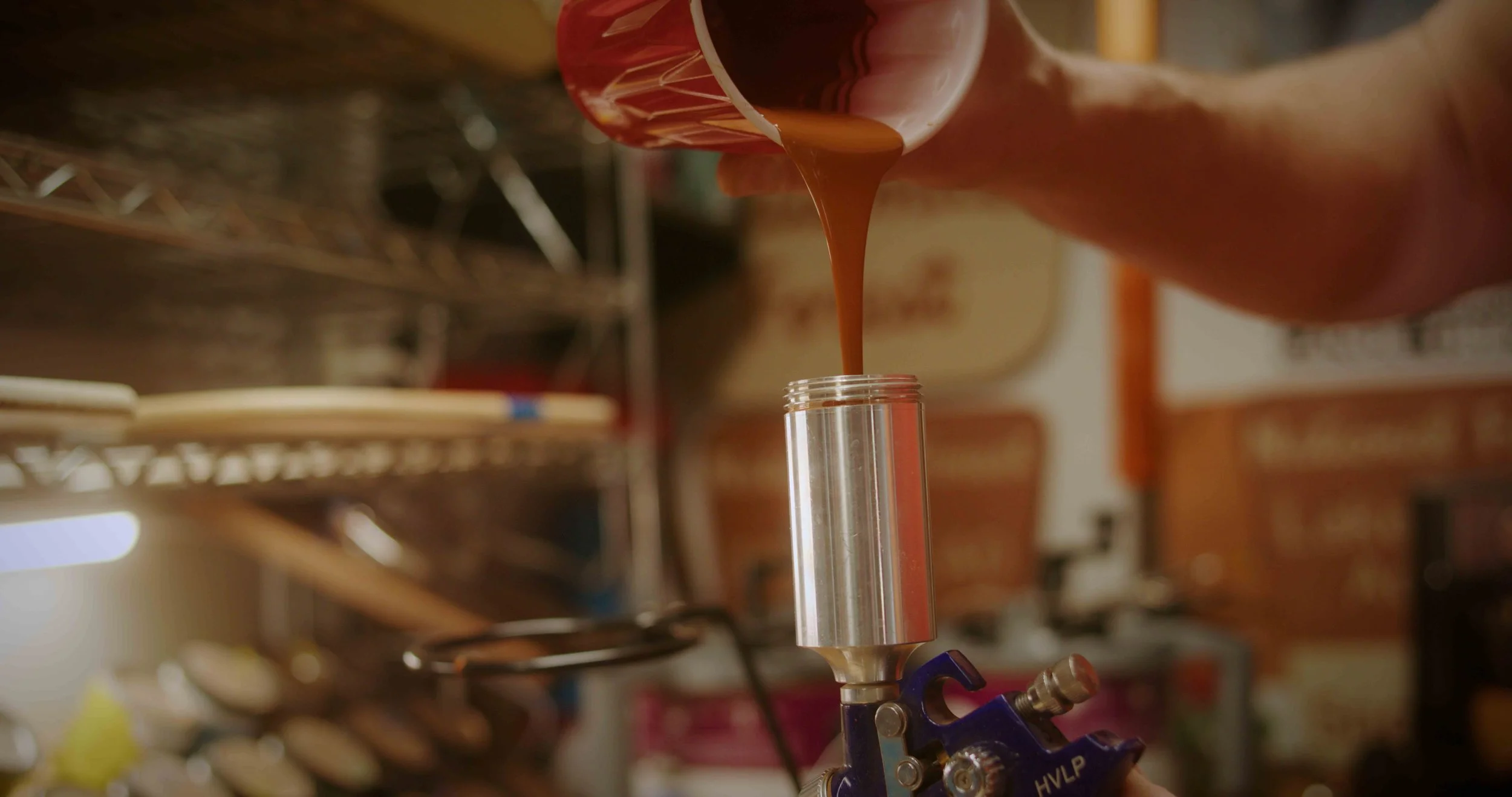 A person is pouring a chocolate liquid from a cup into a metal mold for injection molding.