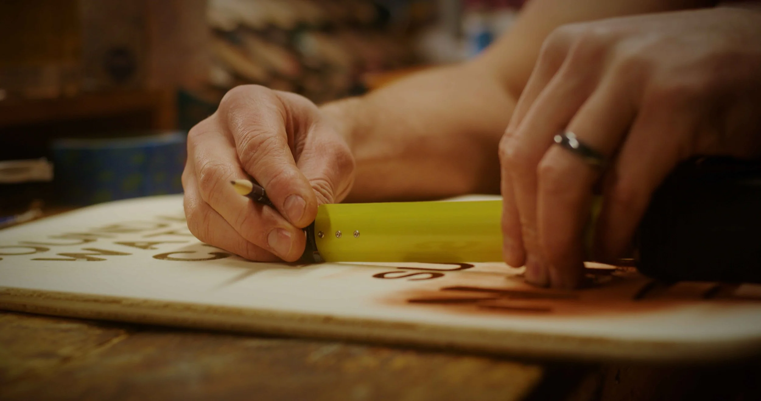 A person using a yellow ruler and a black pen to create or trace black decorative lettering or design on a paper.