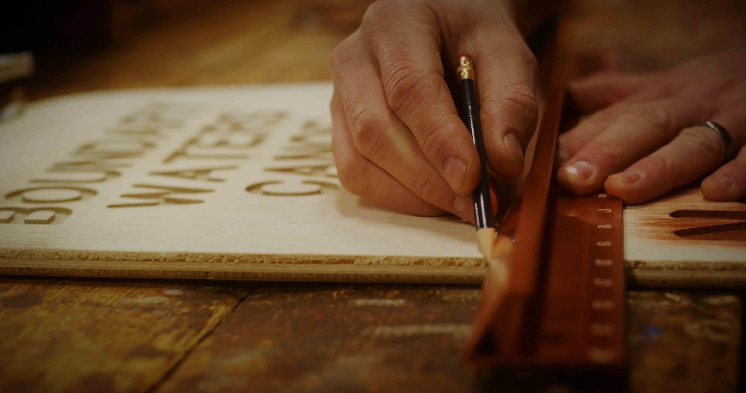 Close-up of a person using a pencil and ruler to trace or cut out wooden letters on a piece of plywood.