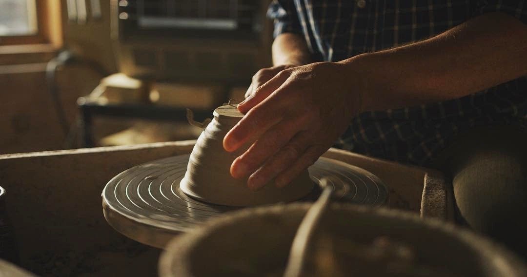 Person shaping clay on a pottery wheel in a workshop.