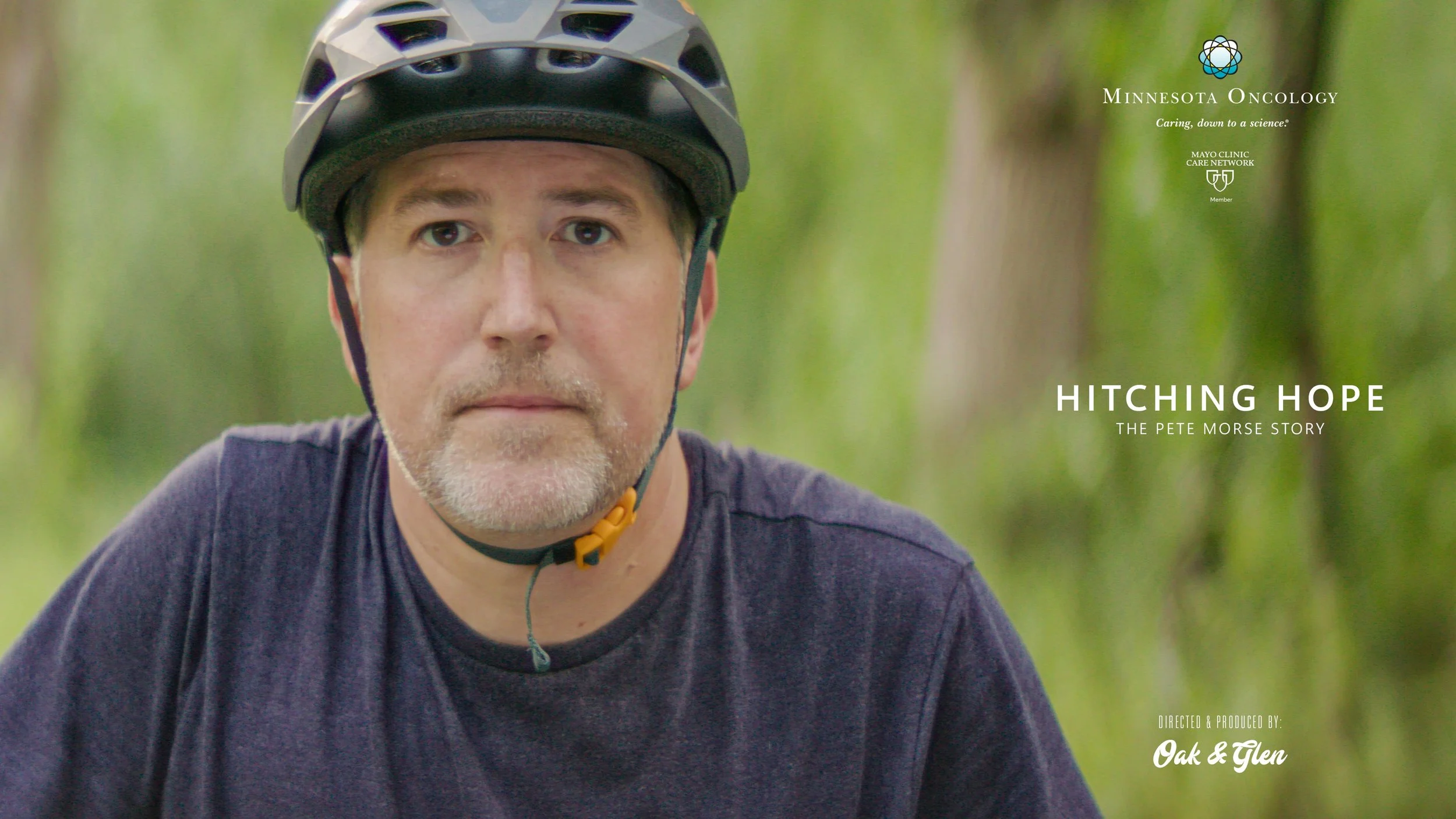 A man wearing a helmet, outdoors in a forest setting, looking directly at the camera, with a serious expression.