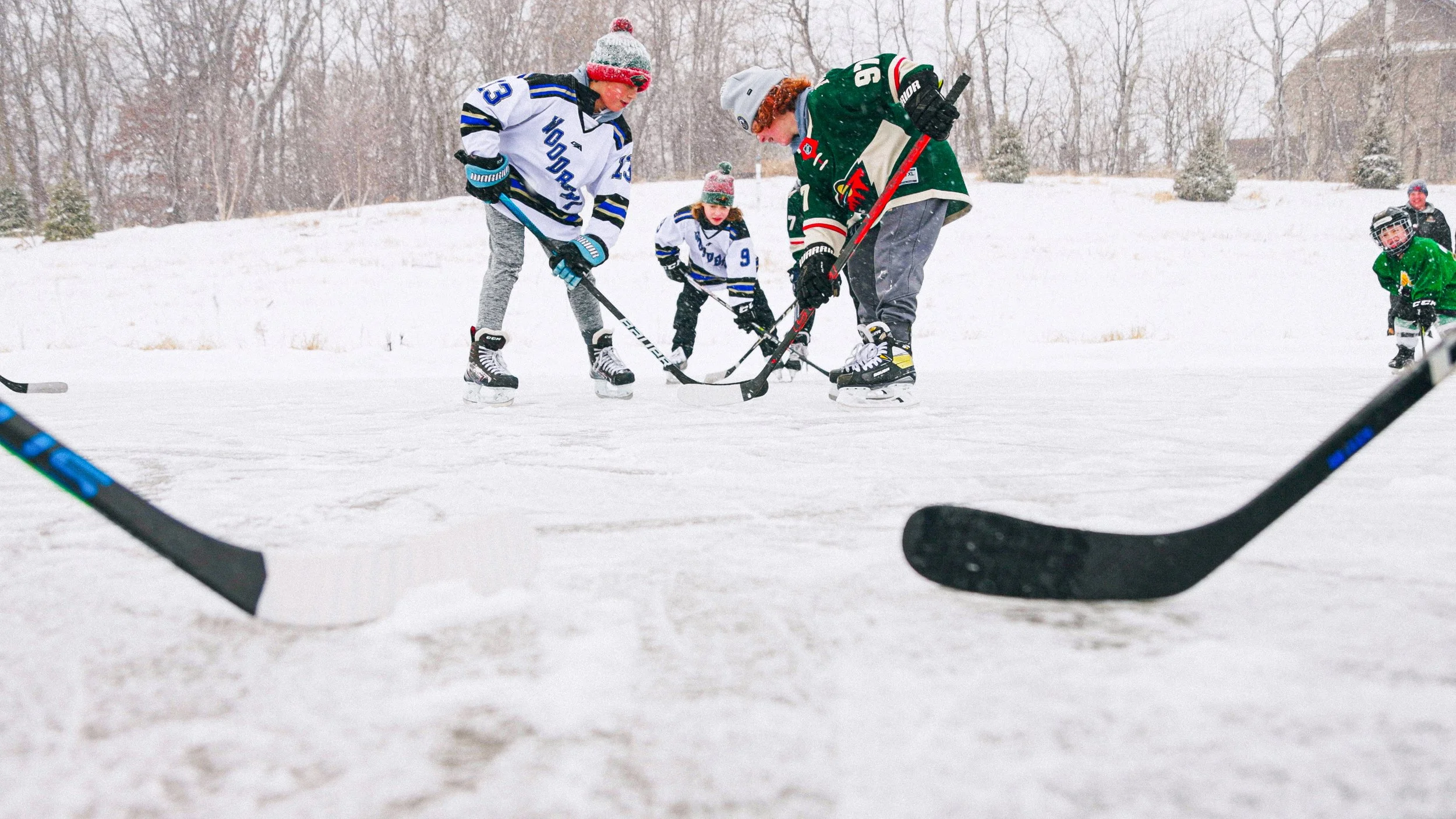 Children playing ice hockey on an outdoor rink in winter, wearing colorful jerseys and winter gear.