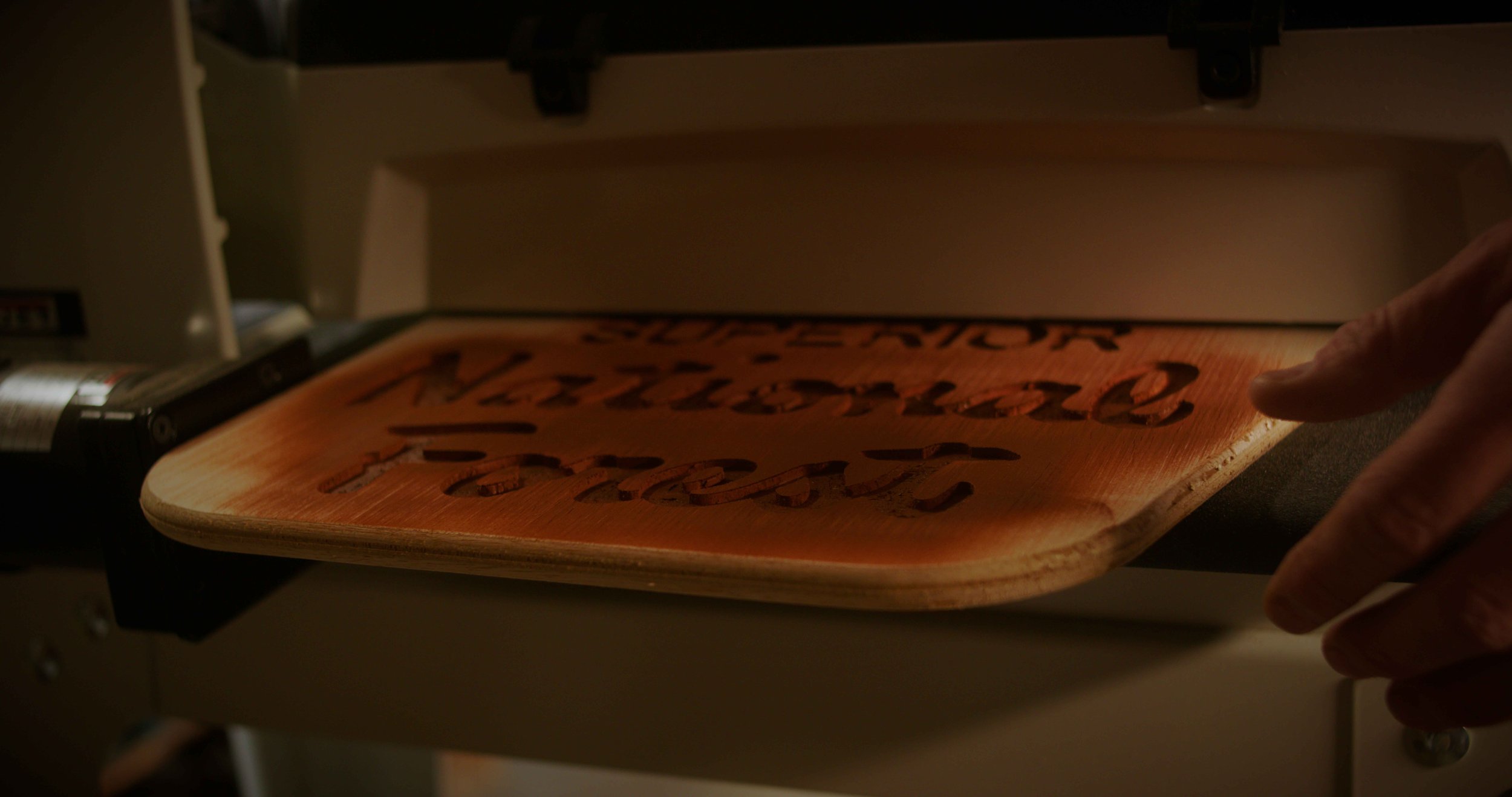 A wood carving of the phrase 'No longer keep the peace' being illuminated by a heat press machine.