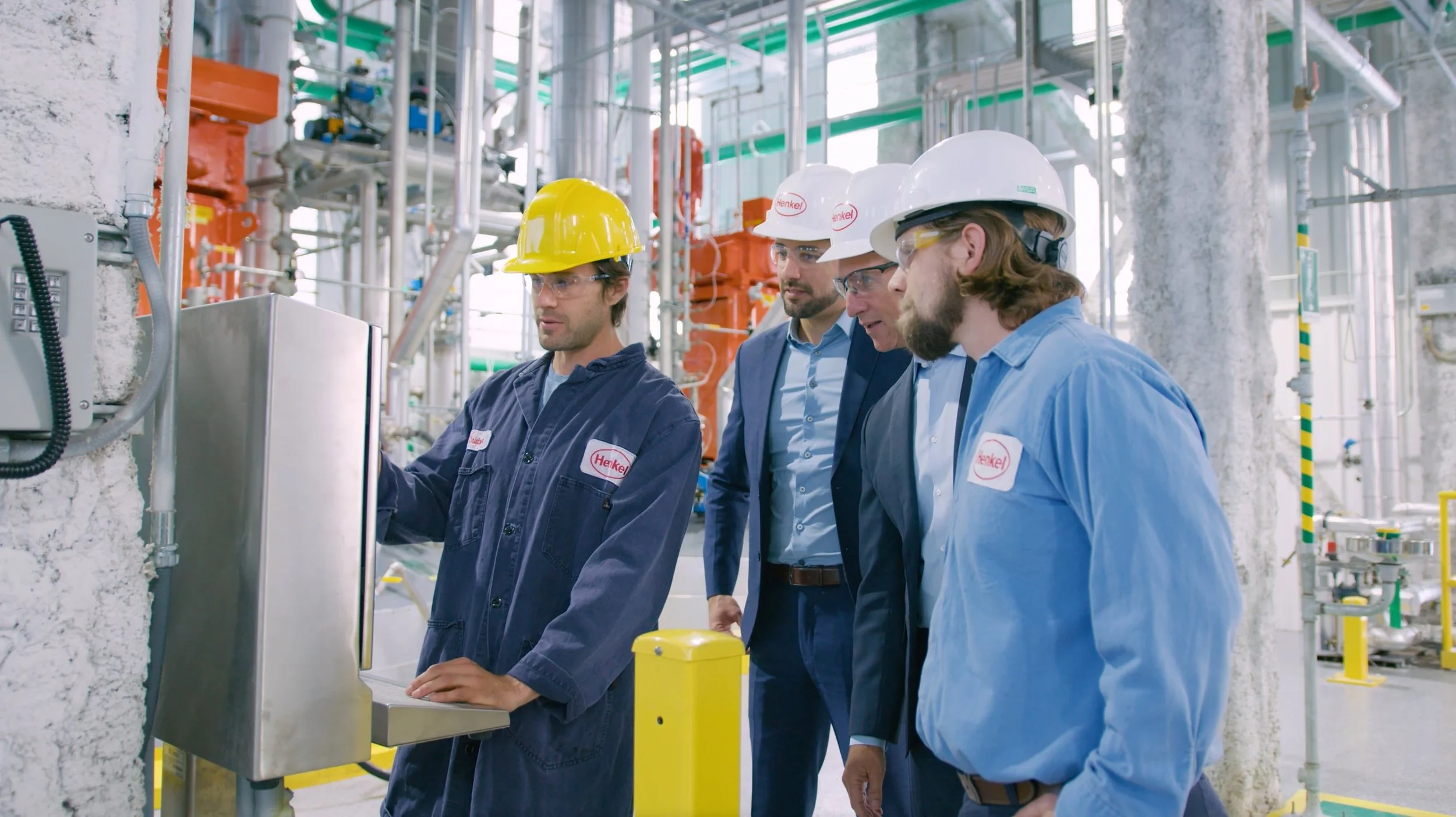 Group of four men in safety helmets and work uniforms inspecting industrial equipment in a factory or processing plant.