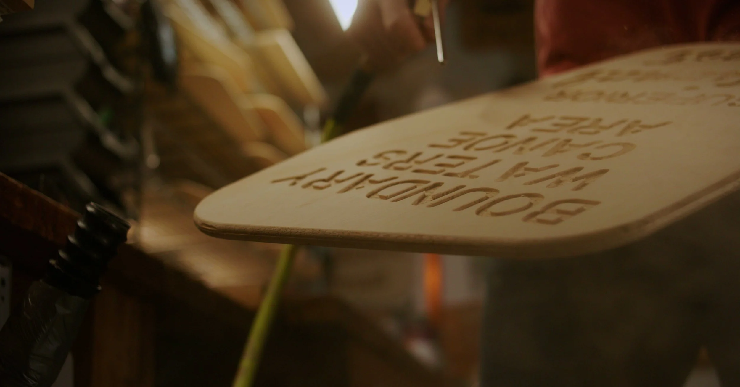 A wooden object with engraved text being carved or crafted in a workshop.