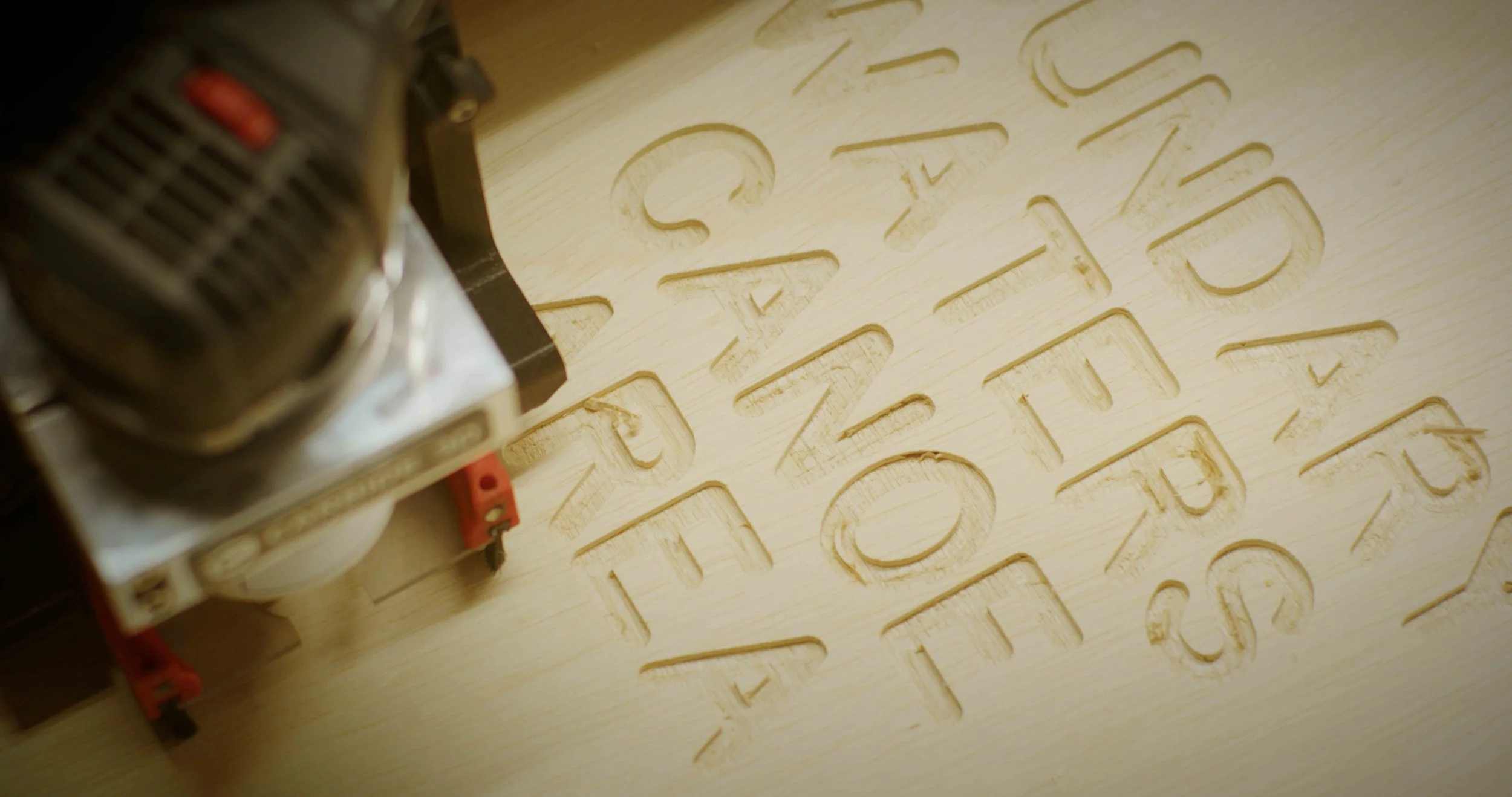 A laser cutter engraving letters into a light-colored wooden surface.