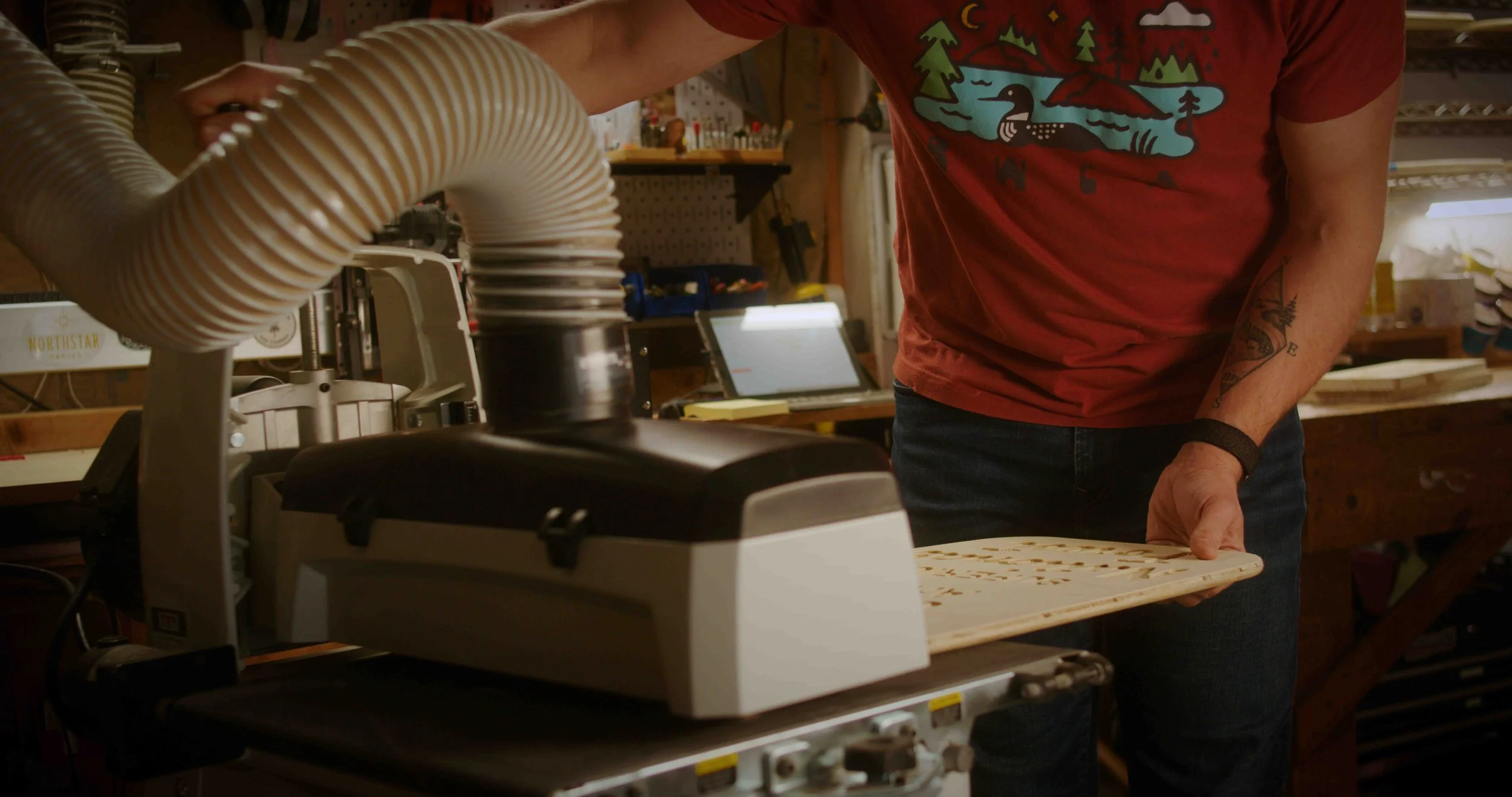 Person using a laser engraving or cutting machine in a workshop, with a tray of material and a laptop in the background.