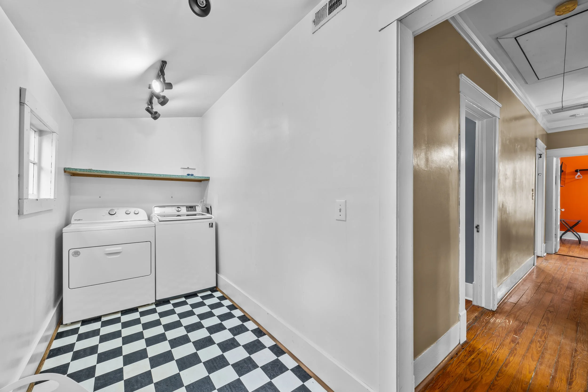 Laundry room with white washer and dryer, checkered black and white floor, white walls, small window, and a shelf above the appliances.