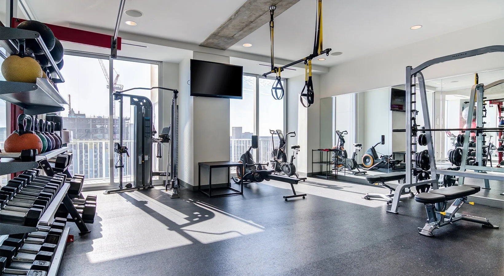 Modern gym with exercise equipment, weights, stationary bikes, and large windows letting in natural light.