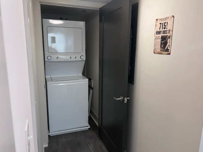 Small laundry nook with stacked white washer and dryer, dark grey cabinet, and wall with vintage poster.