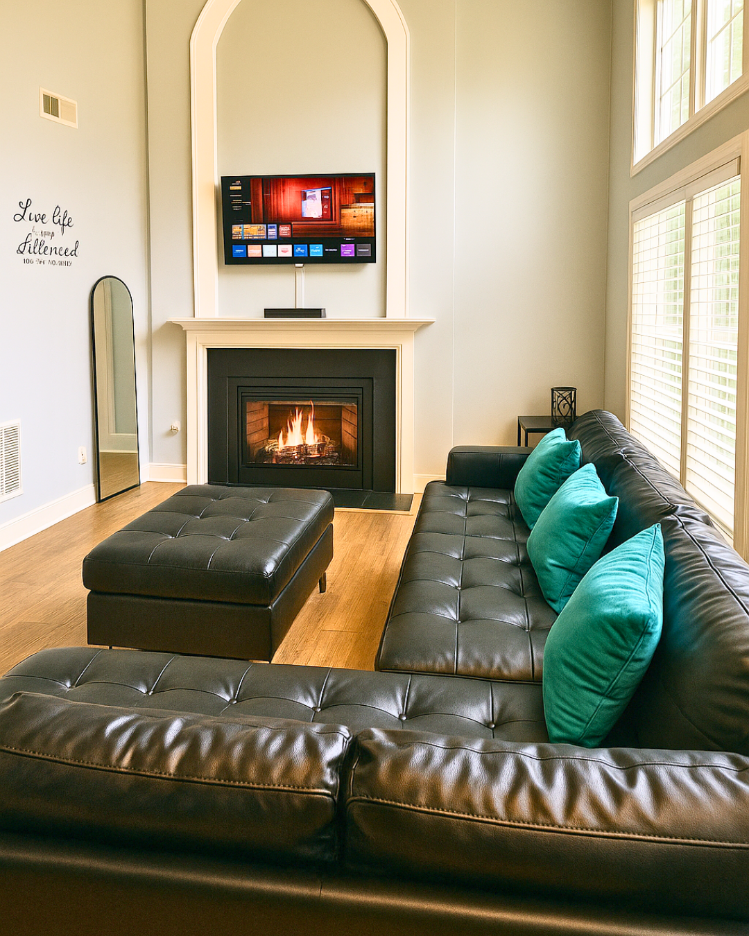 Living room with large window, black sofa with light blue pillows, teal rug, fireplace, and mounted flat-screen TV.