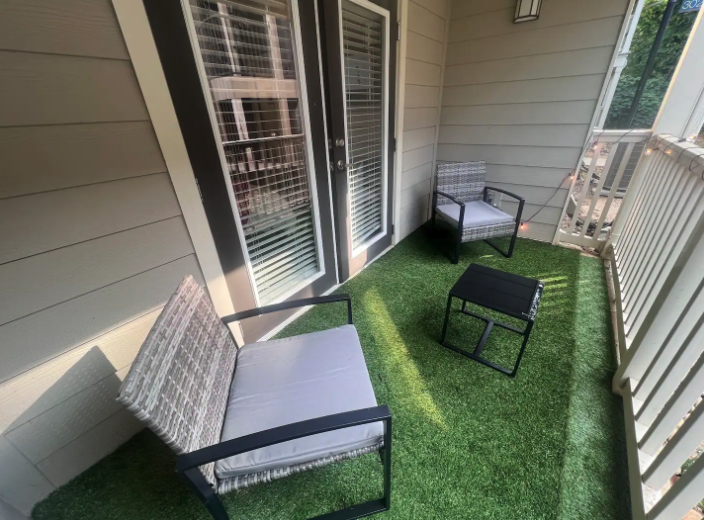 Small balcony with two chairs, a small table, and artificial grass flooring.