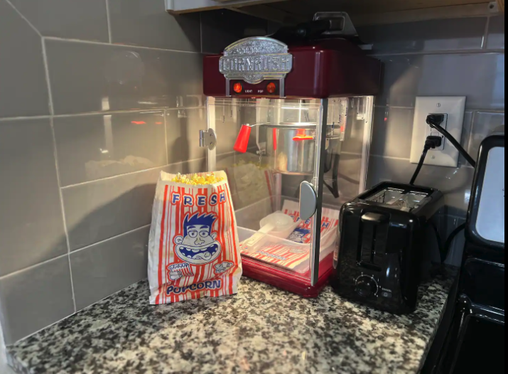 A countertop with a red popcorn machine, a bag of popcorn, and a black toaster in a kitchen setting.