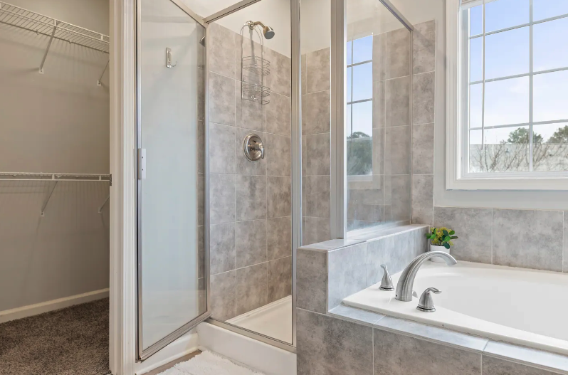 Bathroom with a tiled shower enclosure, a bathtub with a faucet, and a window with a view of trees outside.