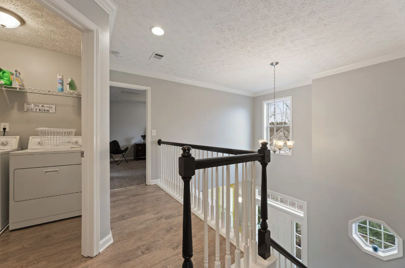 Upper-floor landing area with a staircase, window, hanging light fixture, and a laundry area with washer and shelves.