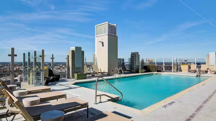 Rooftop swimming pool with lounge chairs and city skyline in the background under a clear blue sky