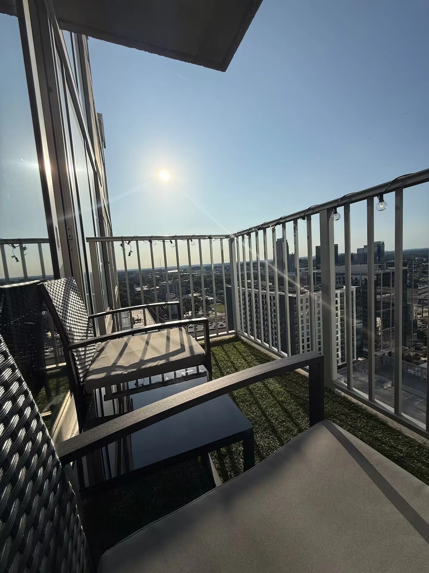 View from a balcony with chairs and a small table, overlooking a cityscape on a clear sunny day.