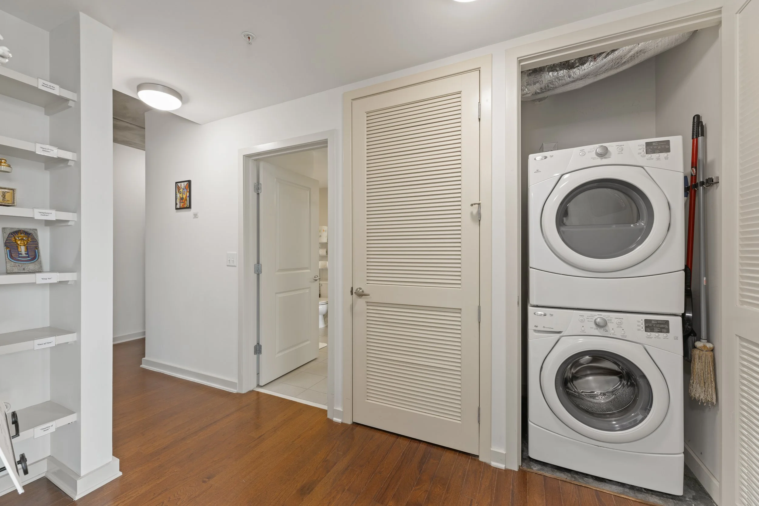 Laundry area with stacked washer and dryer, closet door, hallway, and partially visible bathroom with toilet.